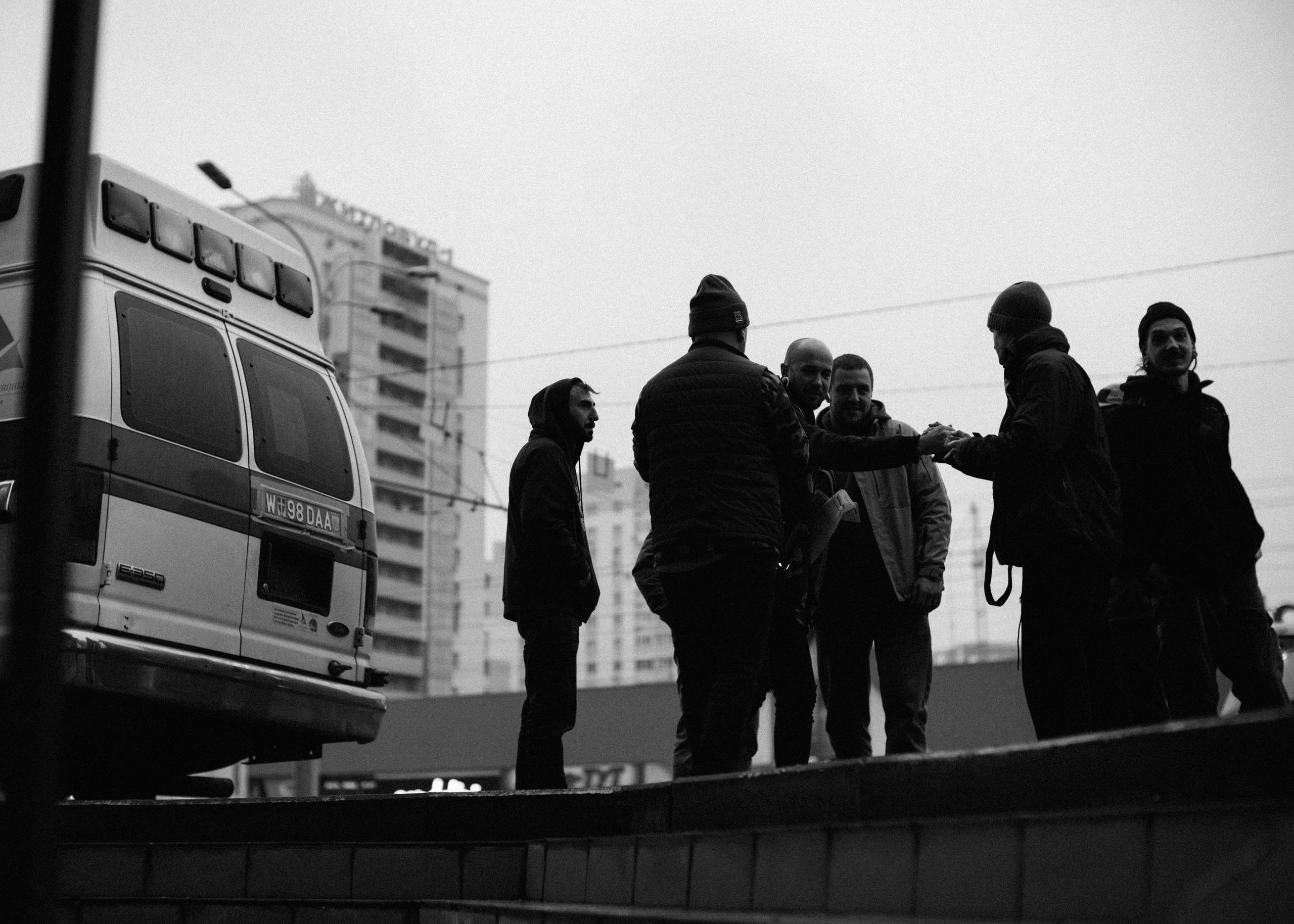 Black and white silhouettes of volunteer team and ambulance truck in front of buildings in Ukraine