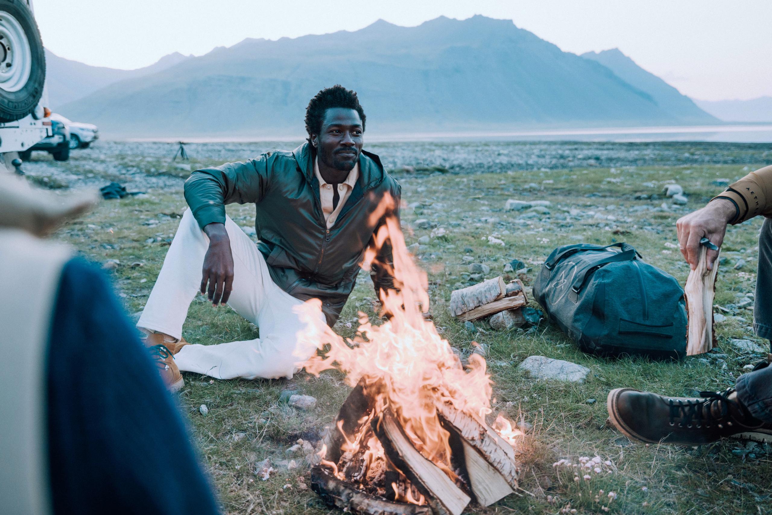 Man lounging on grass next to small campfire in Iceland landscape