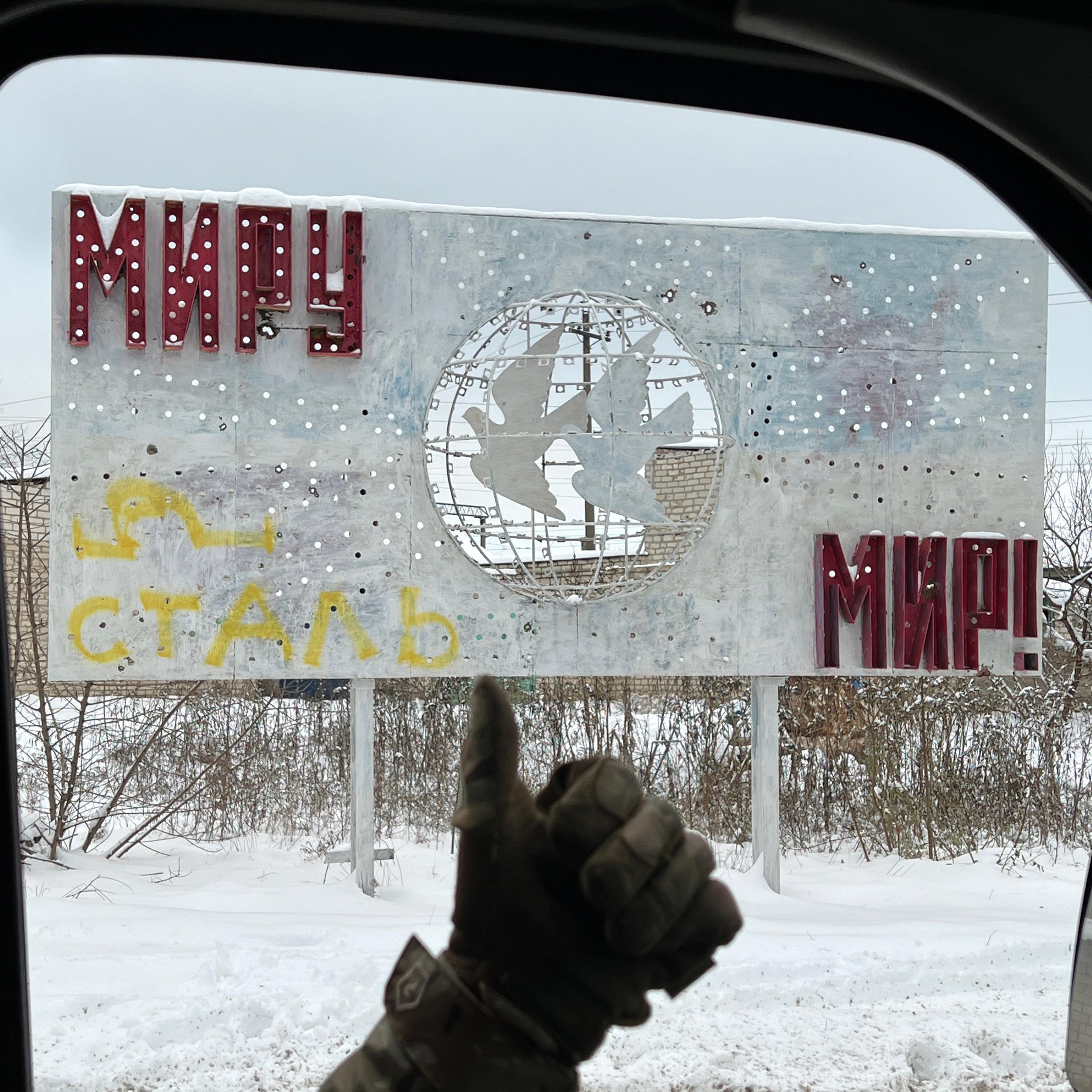 Drivers' hand gives thumbs up in front of old billboard on side of road in Ukraine