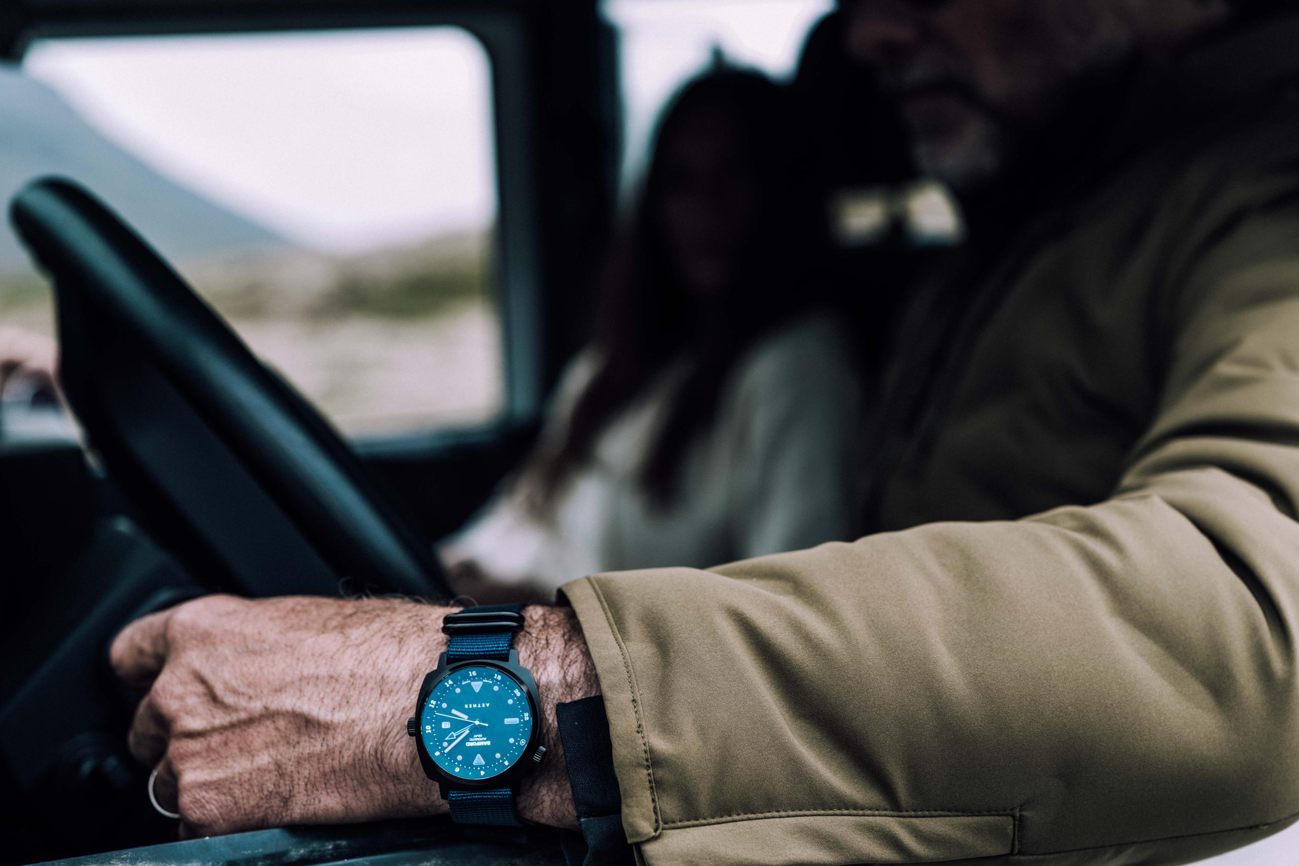Closeup of man sitting in truck with AETHER + Bamford GMT watch showing