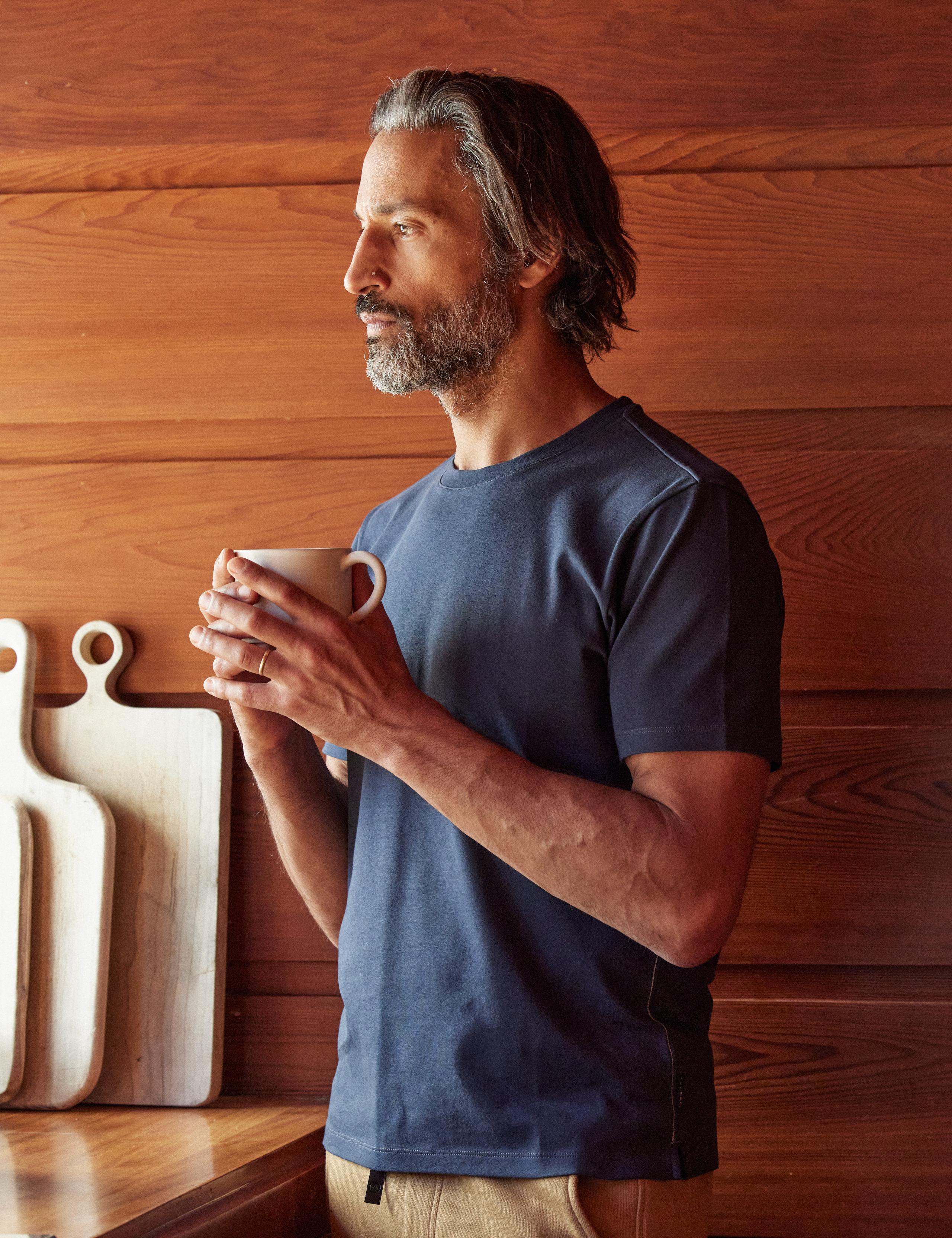 Man wearing Relaxed-Fit Crew Tee and holding a cup of tea in kitchen of mid-century home