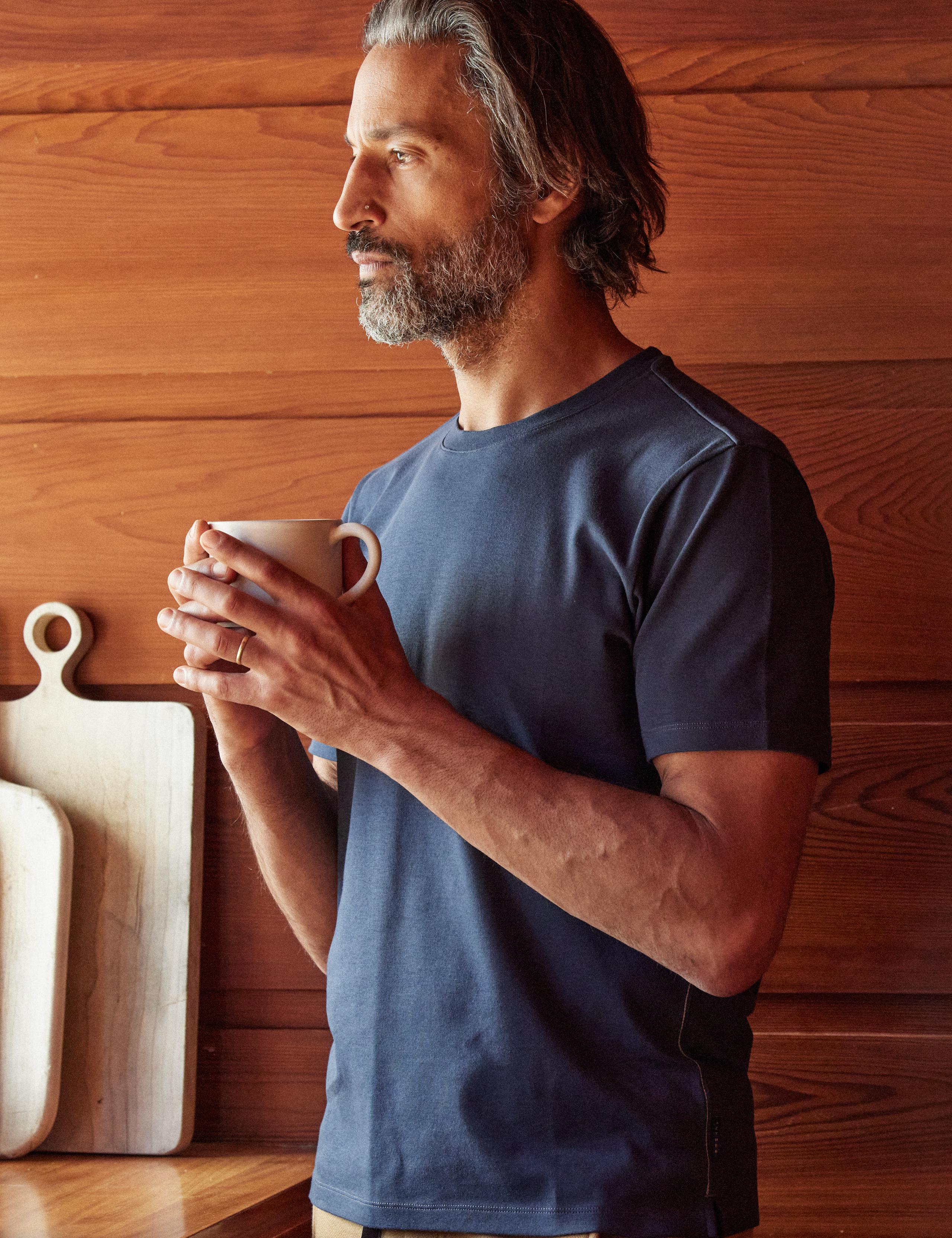 Man holding cup of coffee inside wood paneled mid-century home