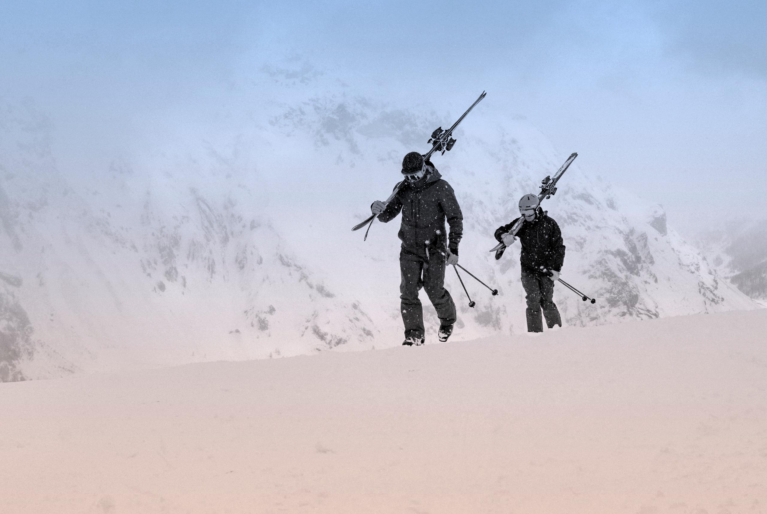 Black and white photo of two skiers walking across a snowy mountain
