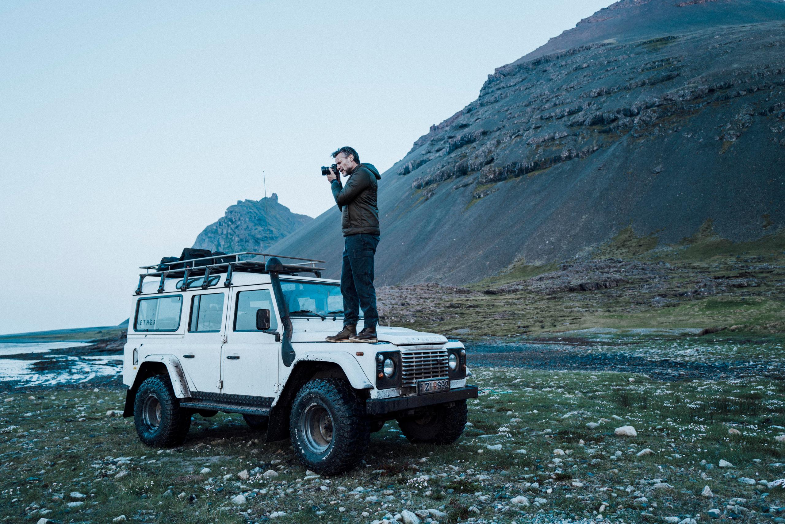 Man taking photo with camera standing on white Defender in front of Iceland landscape
