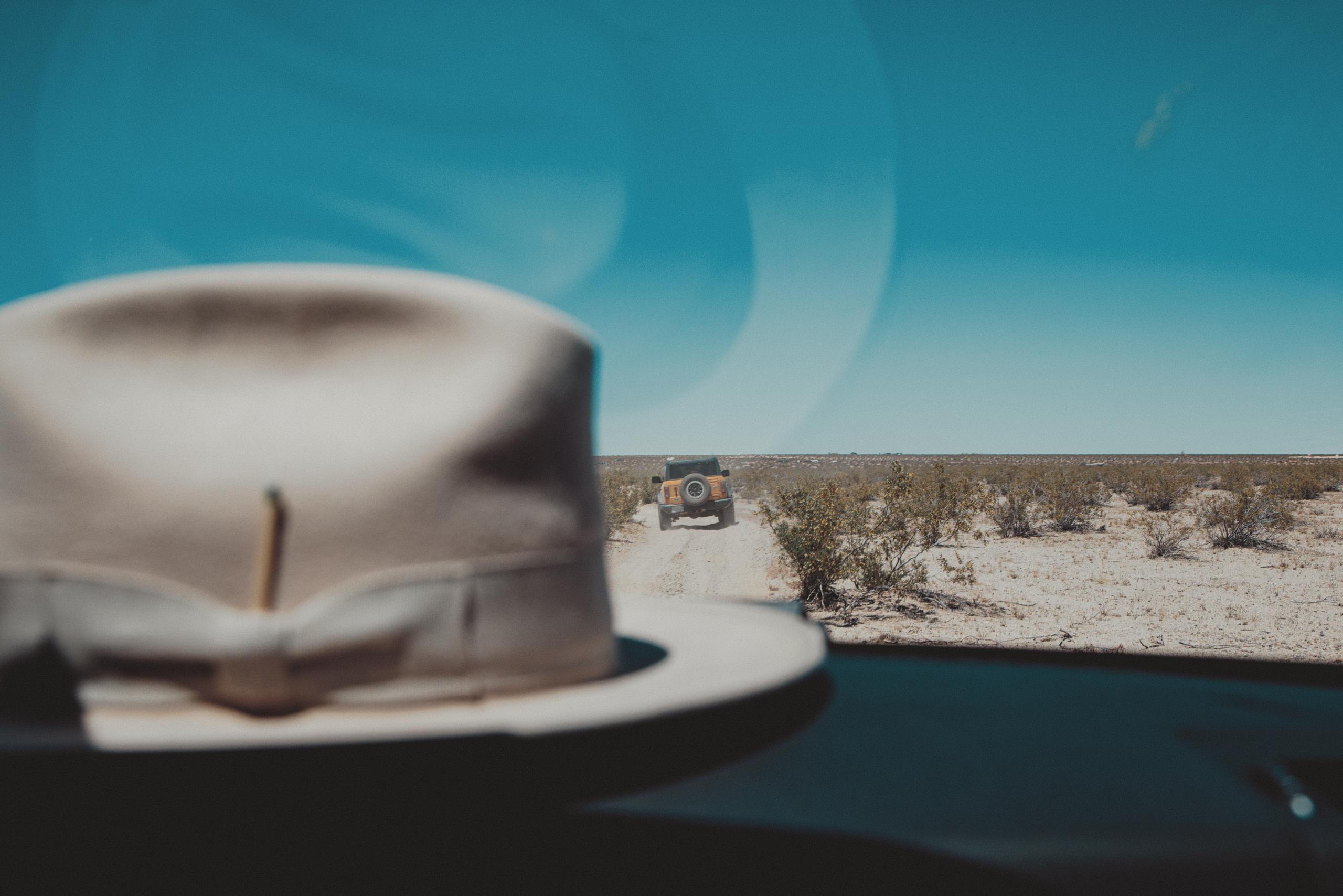 Hat on the dashboard overlooking car driving down dirt road in Joshua Tree