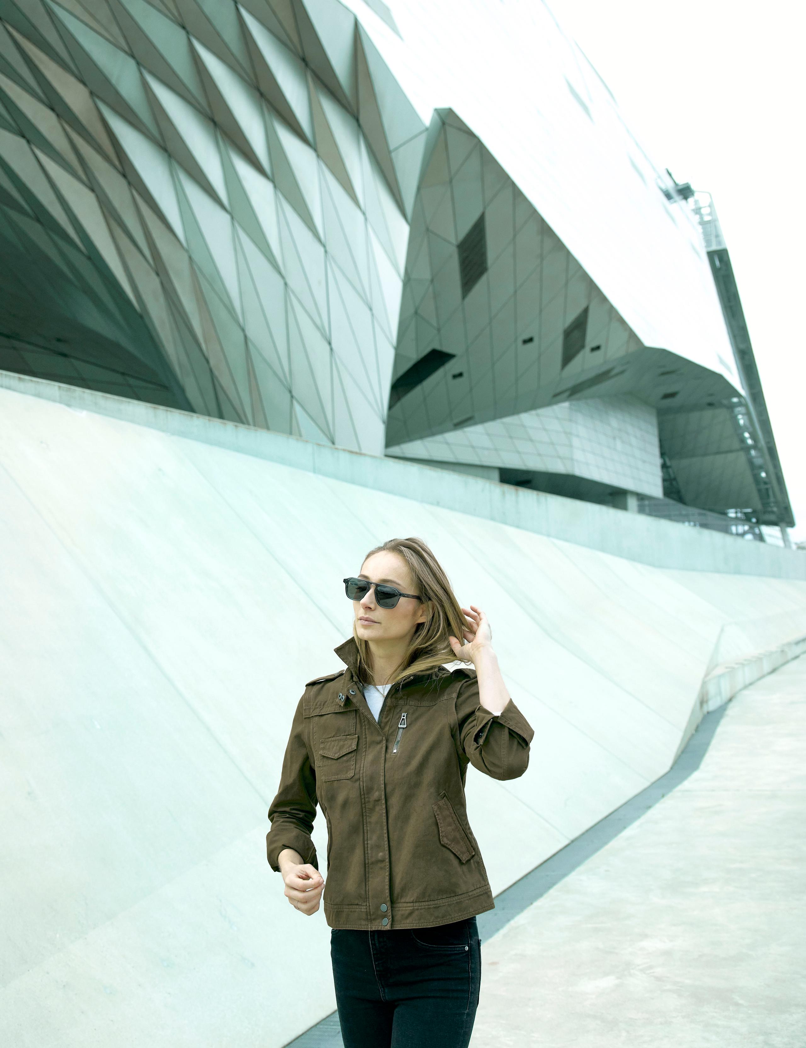 Woman wearing the Sahara Cotton Jacket walking in front of modern building in Lyon, France