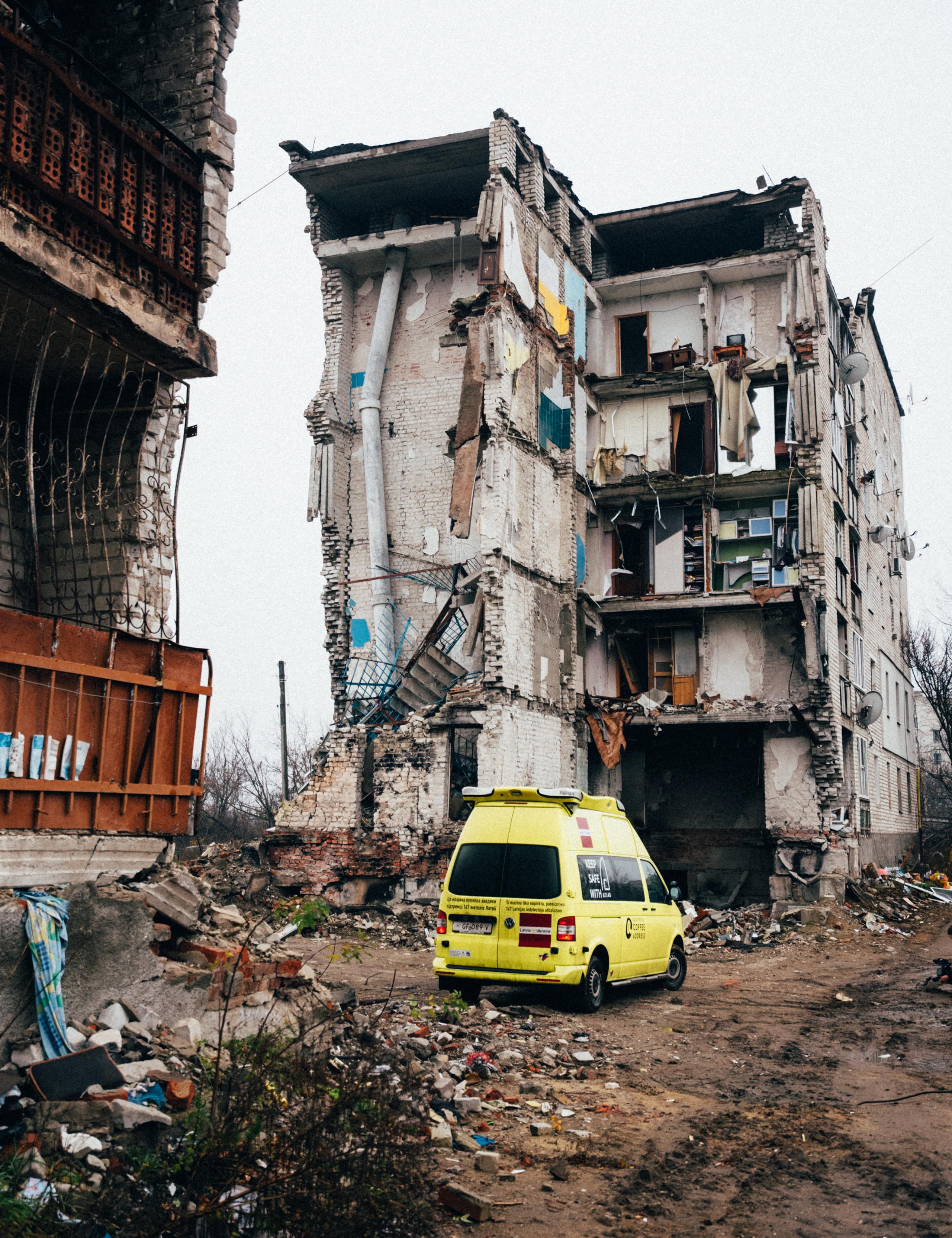 Yellow volunteer truck parked in front of destroyed building in Ukraine