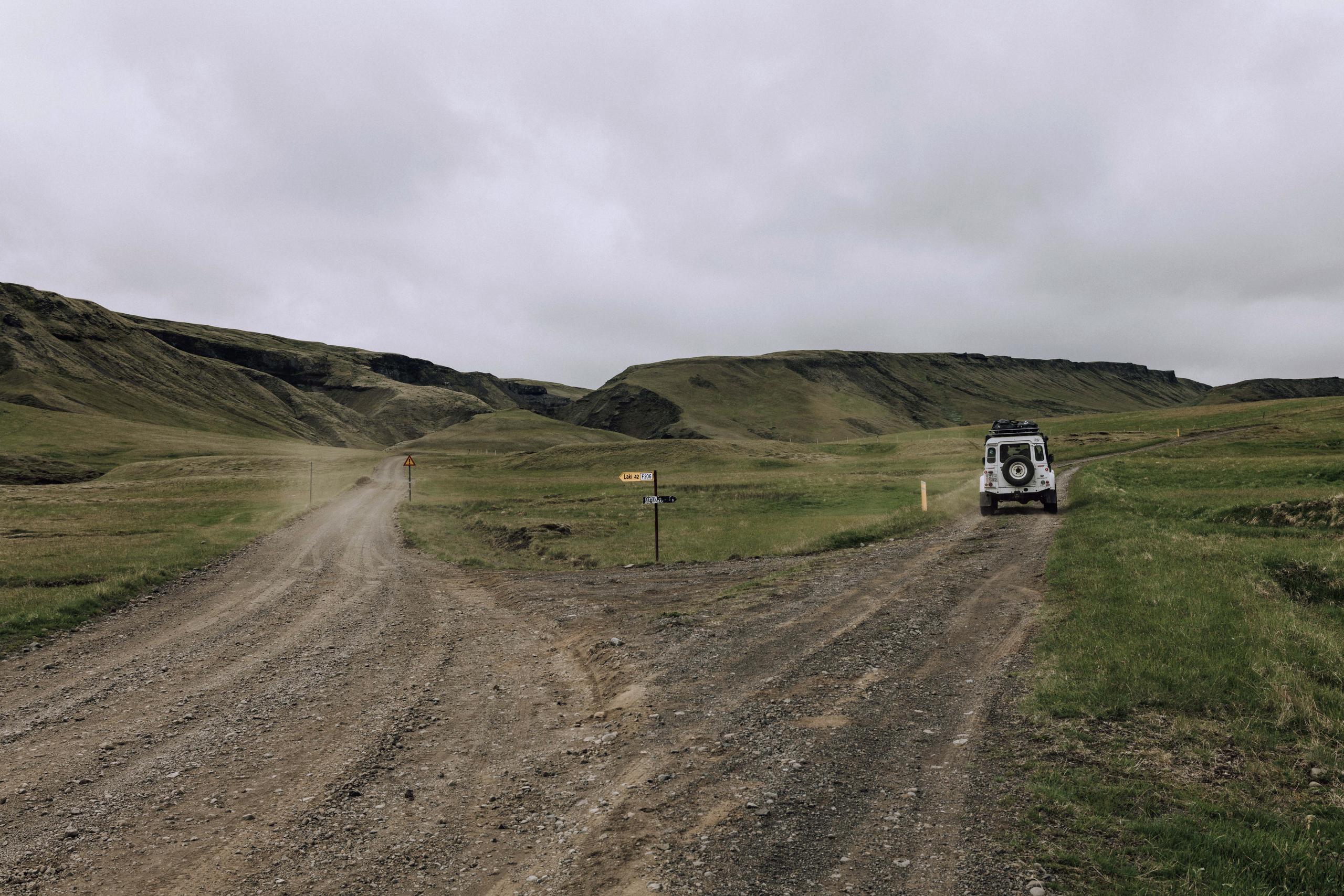 White Defender driving down right dirt road after a fork in the road