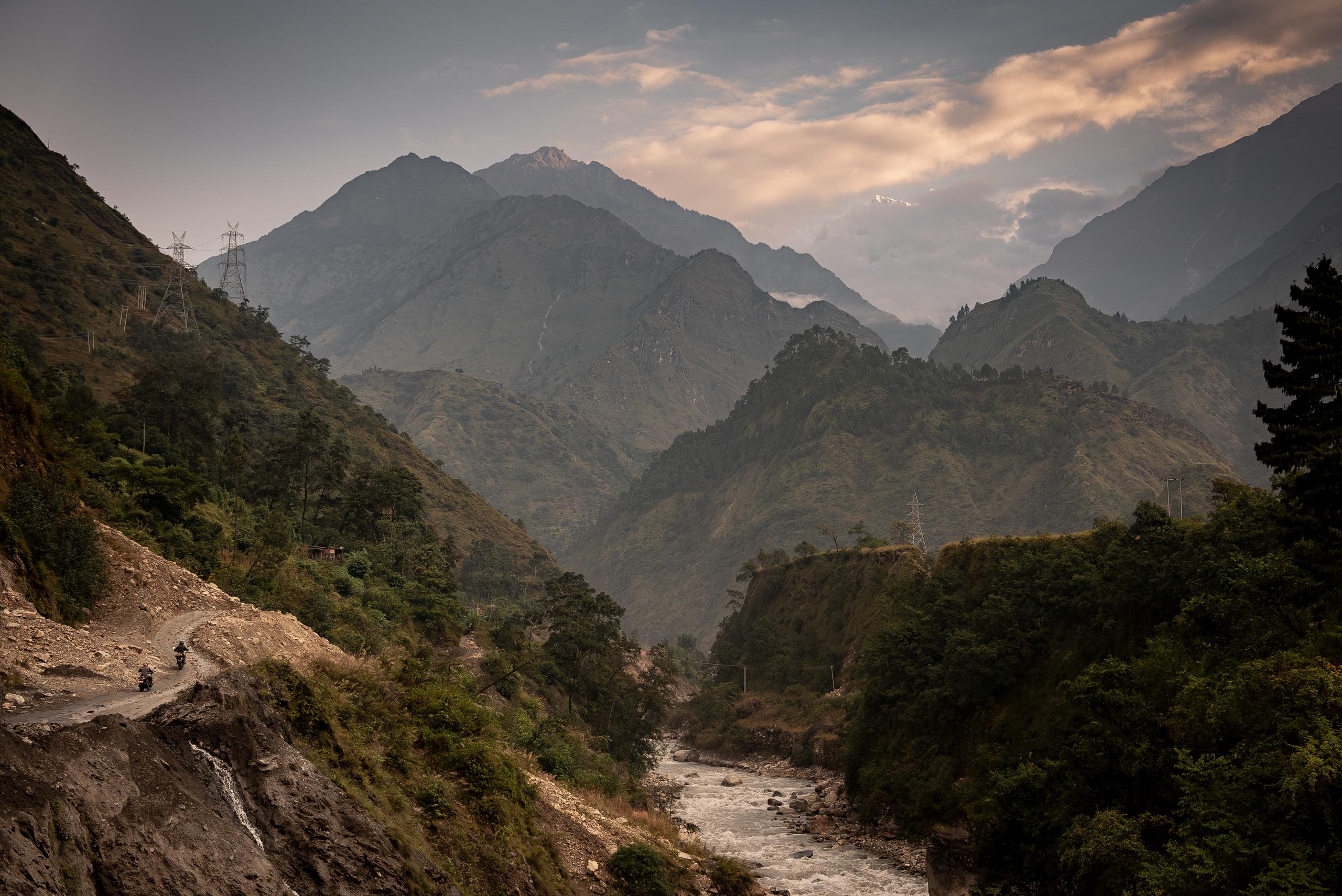 Two motorcyclist on mountaineous dirt road alongside river in Nepal 