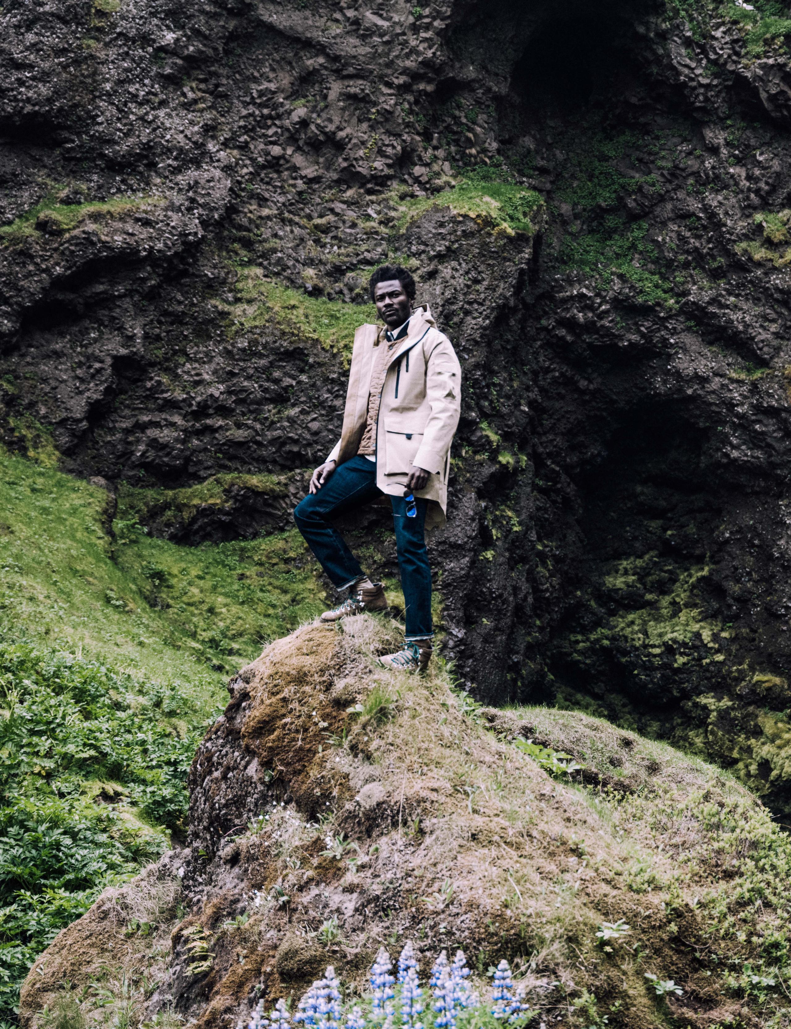 Man wearing AETHER + Mackintosh Field Parka on rocky terrain next to waterfall in Iceland