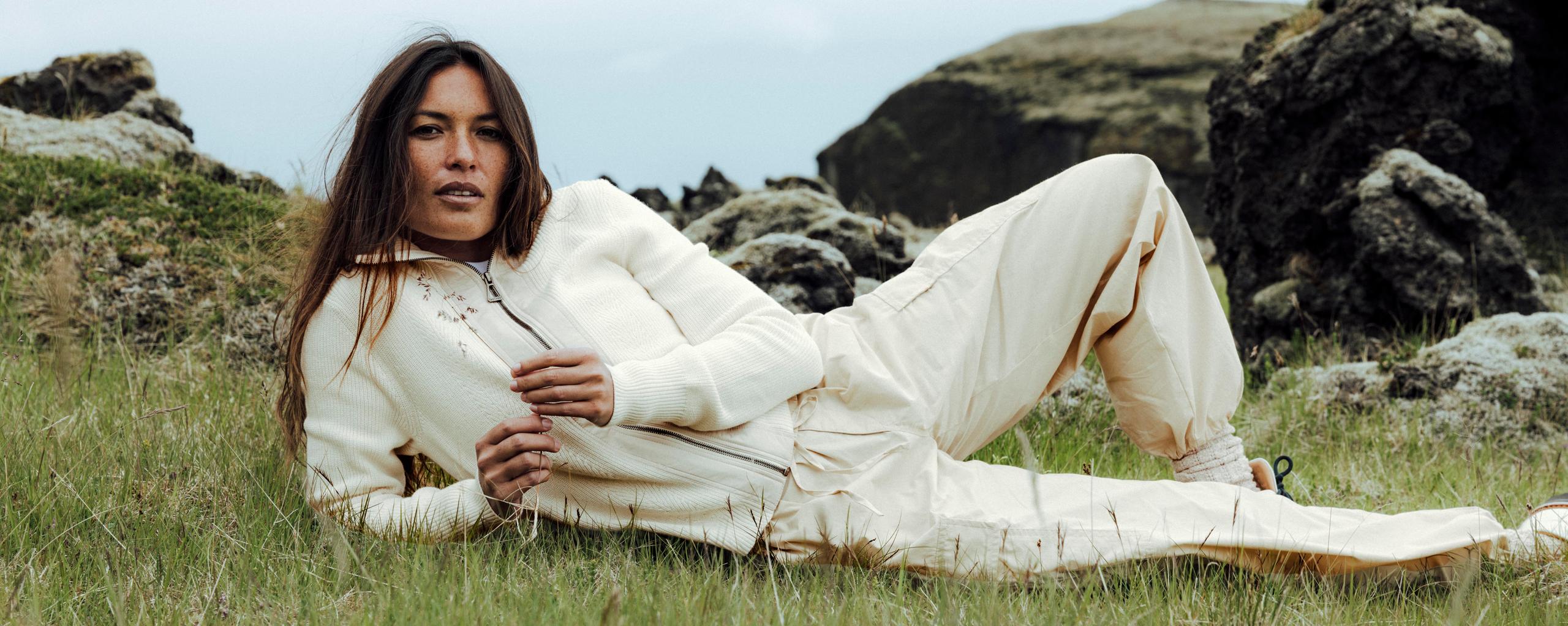 Woman laying on grass in white outfit alongside Iceland coast