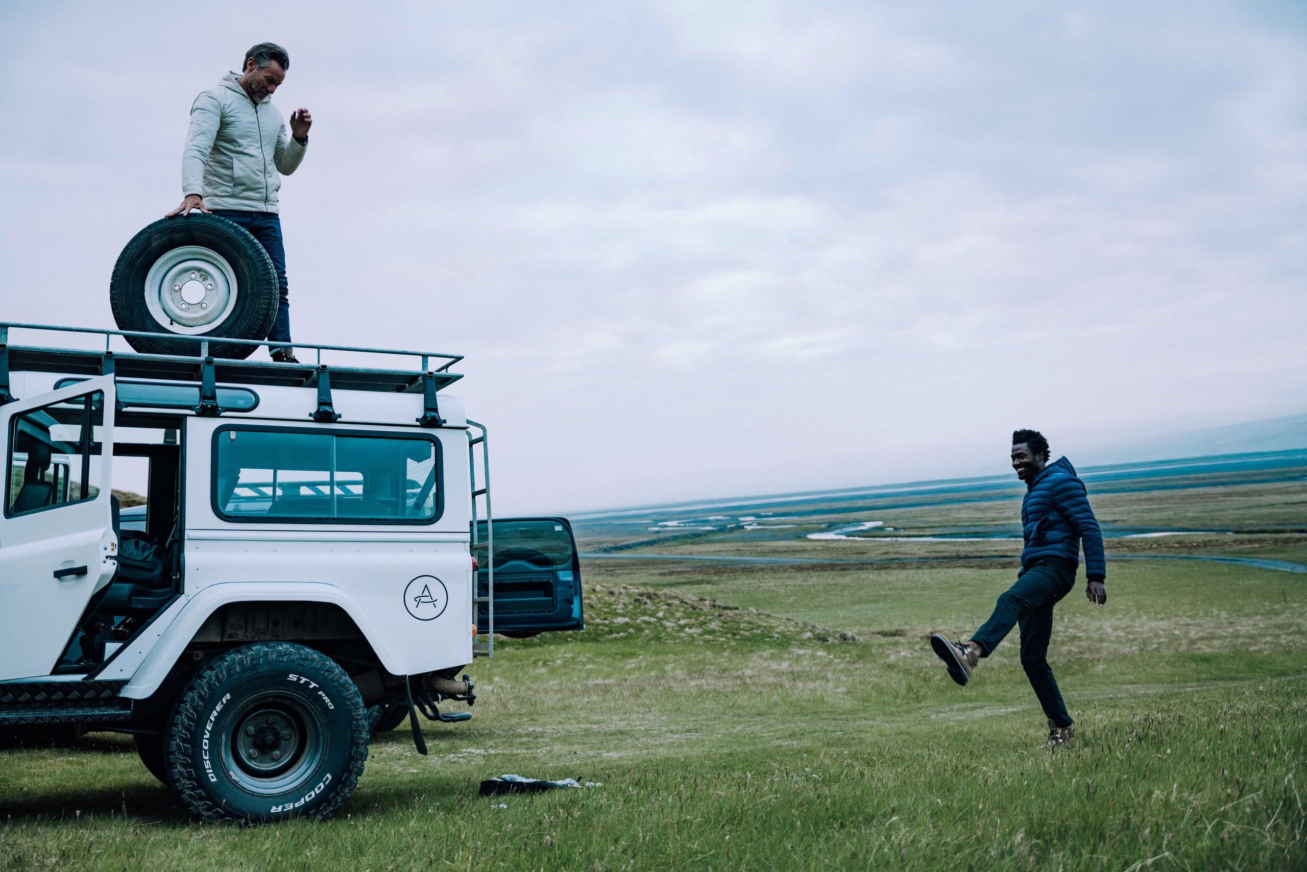 Two men in Iceland landscape alongside white Defender changing the tire