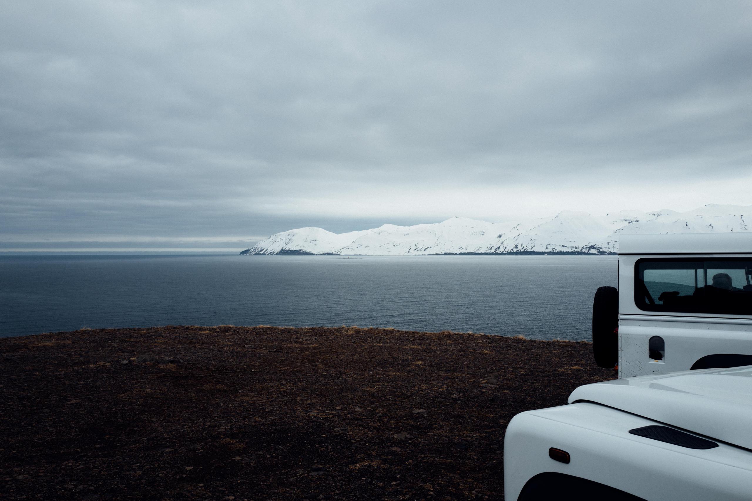 Two white Land Rovers in foreground and Iceland seascape in the background
