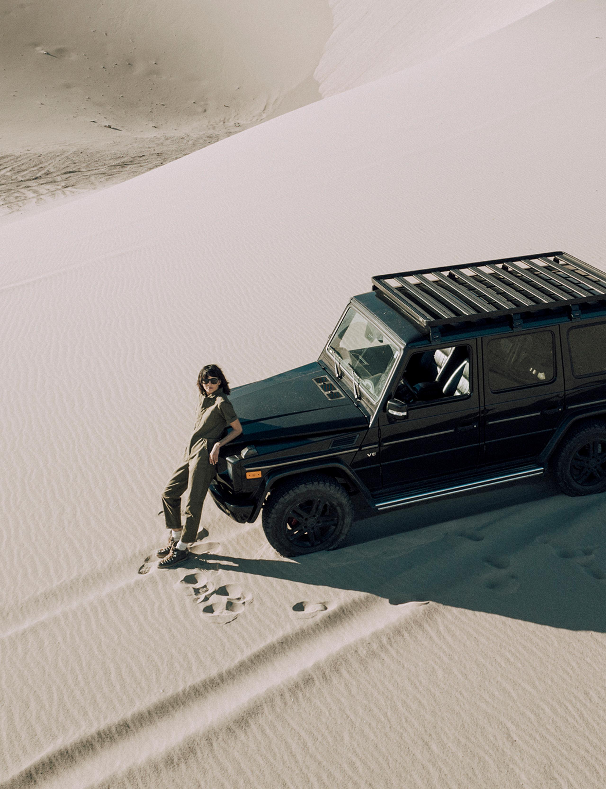 Aerial view of woman standing next to black G wagon in sand dune landscape