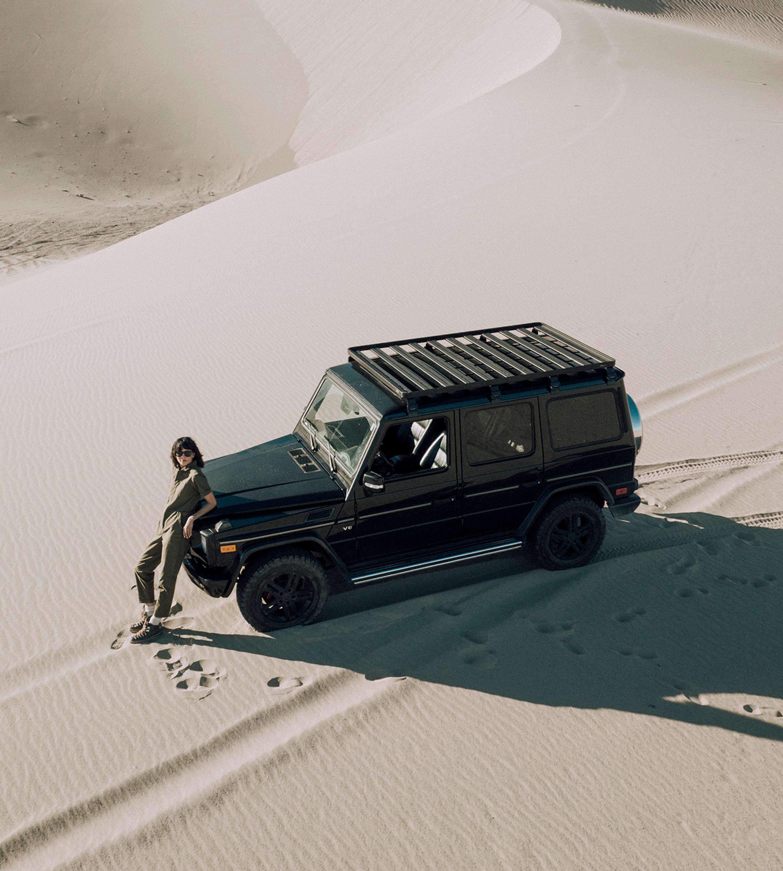 Aerial view of woman leaning on front of Land Rover in the middle of desert sand dunes