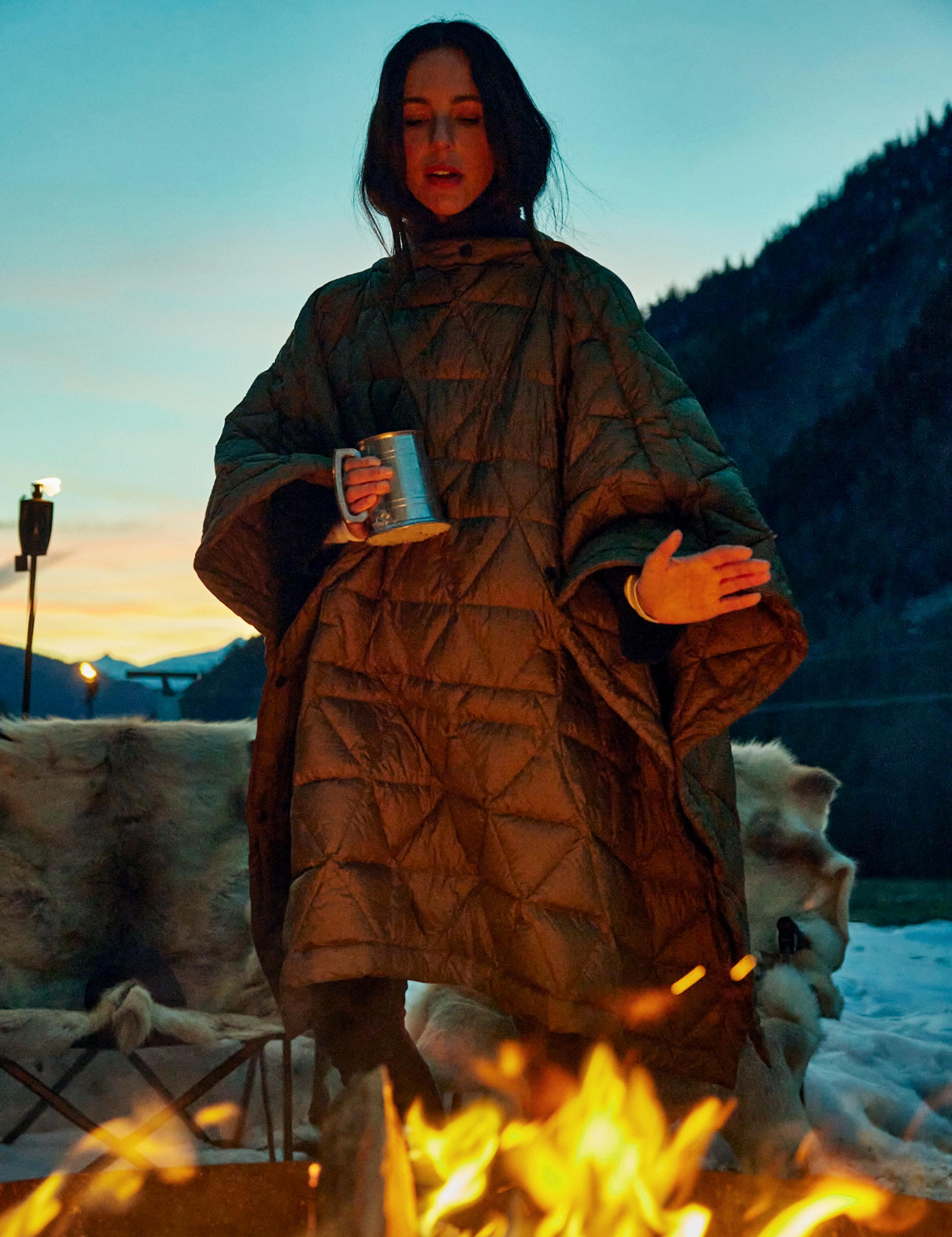 Girl wearing Down Poncho in front of campfire