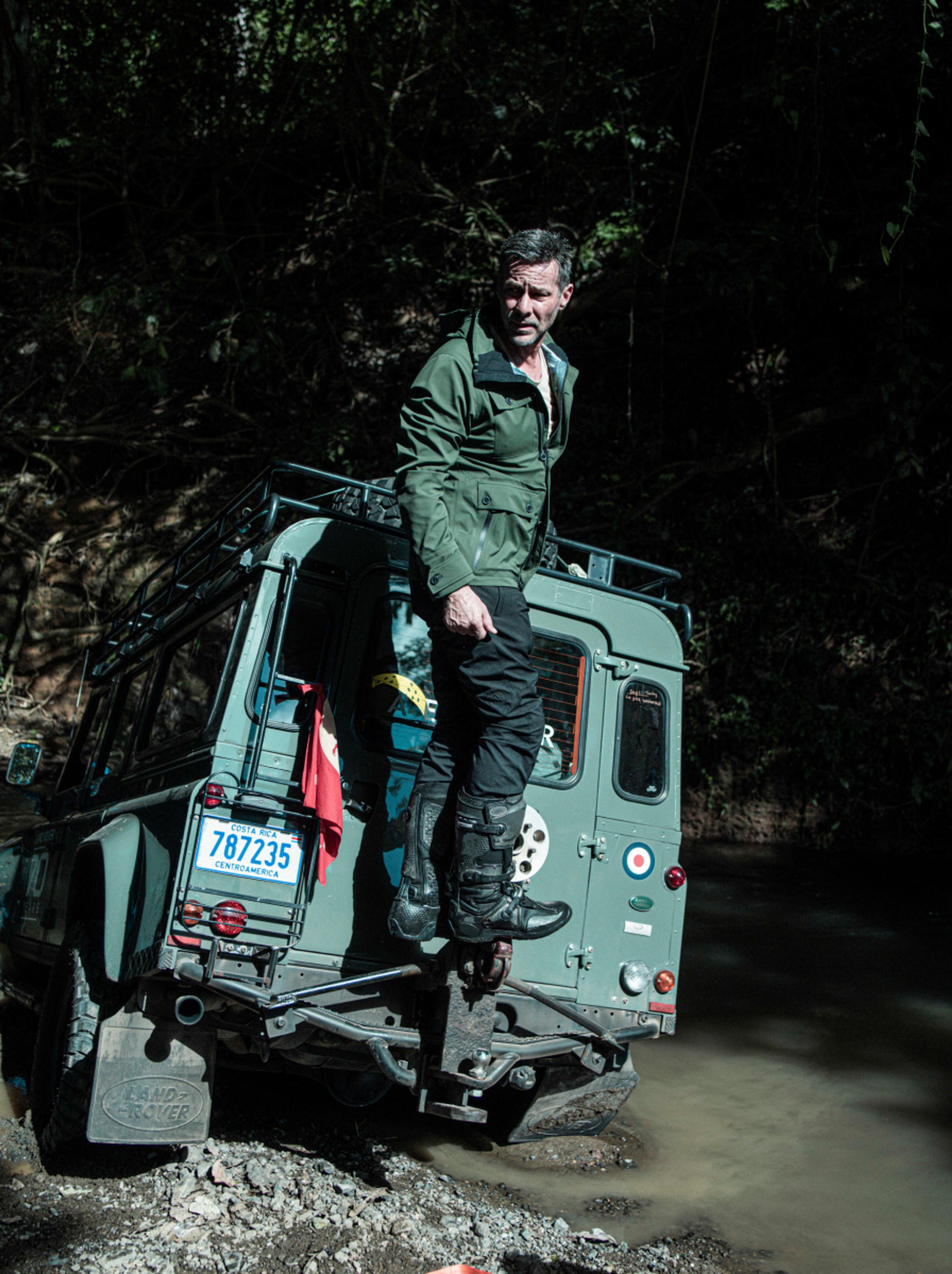 Man standing on back of Land Rover that's stuck in a river in Costa Rica