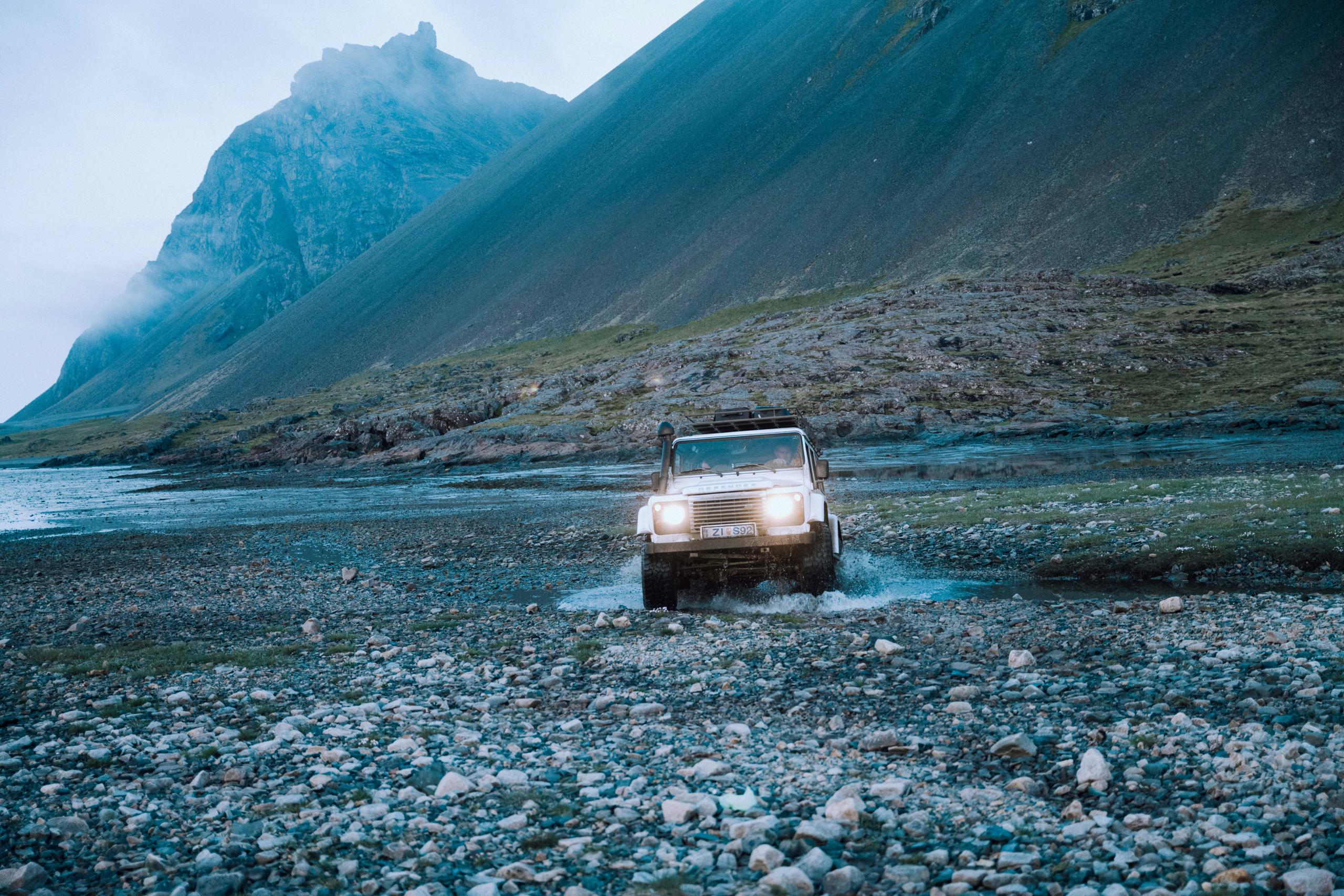 White Defender truck driving across low river in rocky Iceland terrain