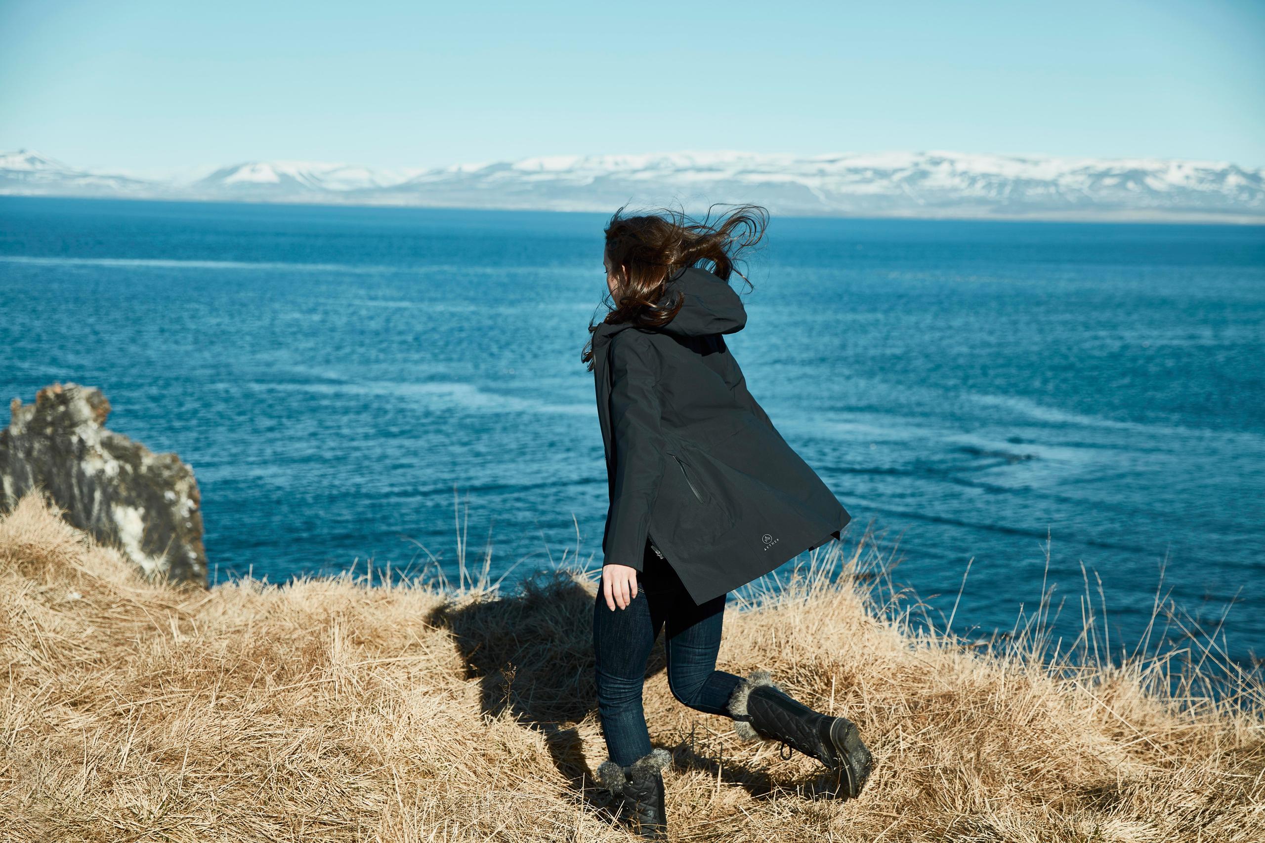 Women in jacket running along edge of cliff with the sea in the background in Iceland 