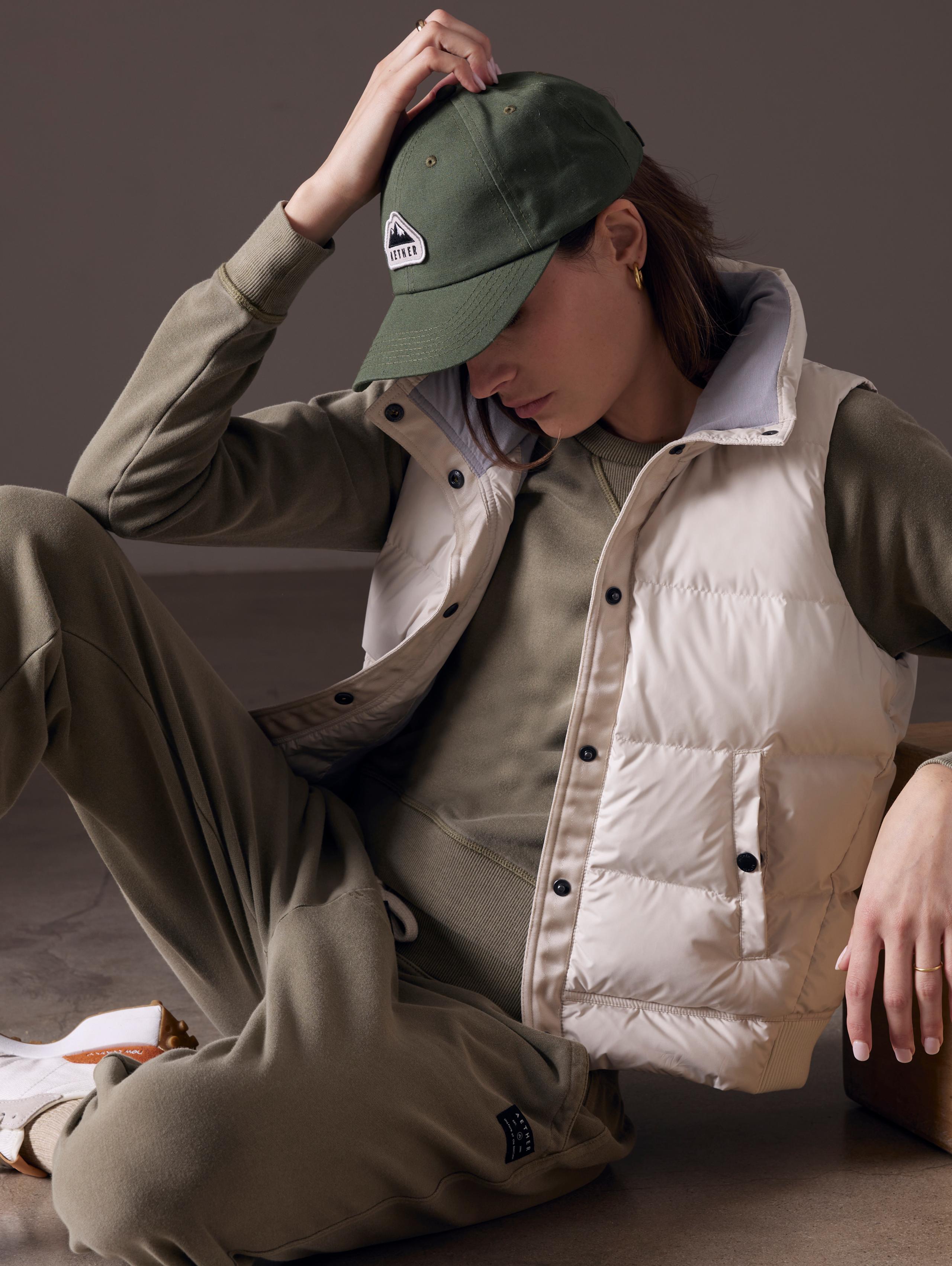 Woman in studio leaning on apple box with Anning Vest layered over Solstice sweatshirt and pants