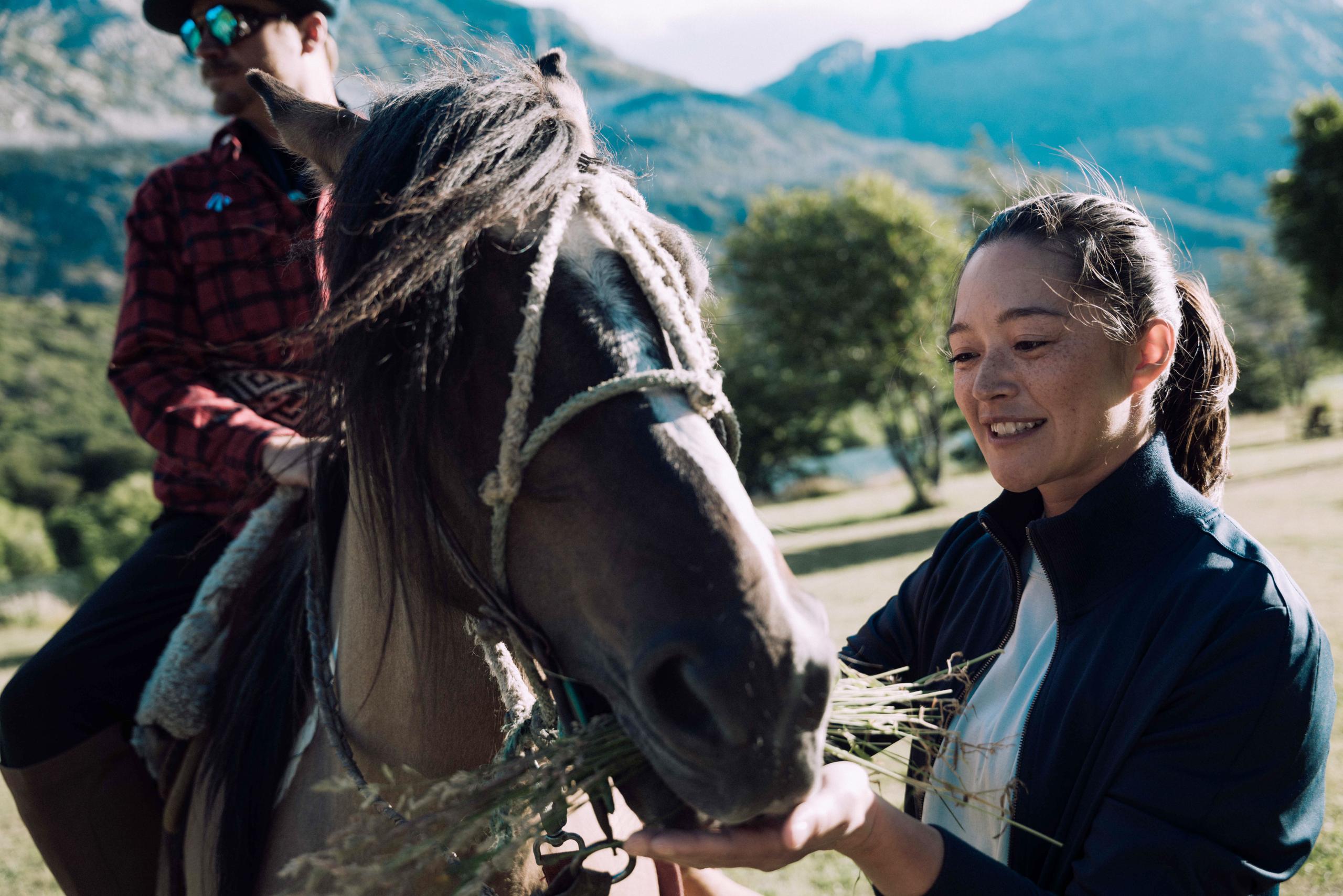 Woman feeding hay to horse in field in Patagonia, Chile