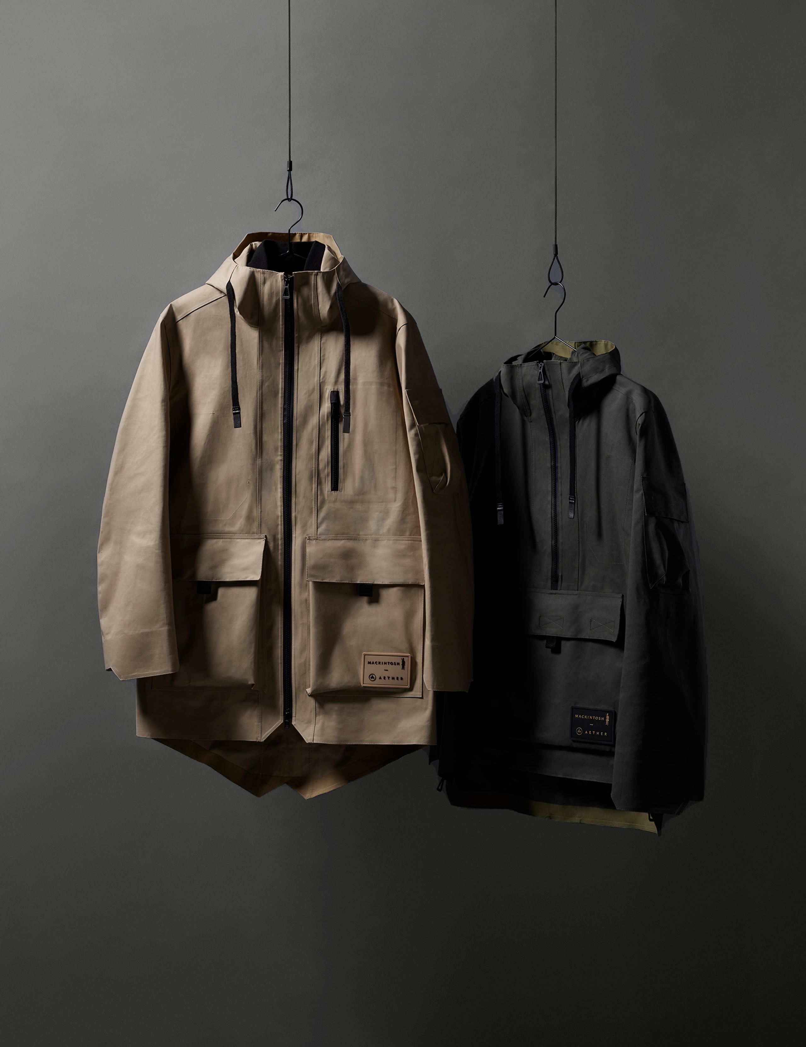 Studio photo of Mackintosh Field Jacket and Anorak hanging from metal hangers against dark background