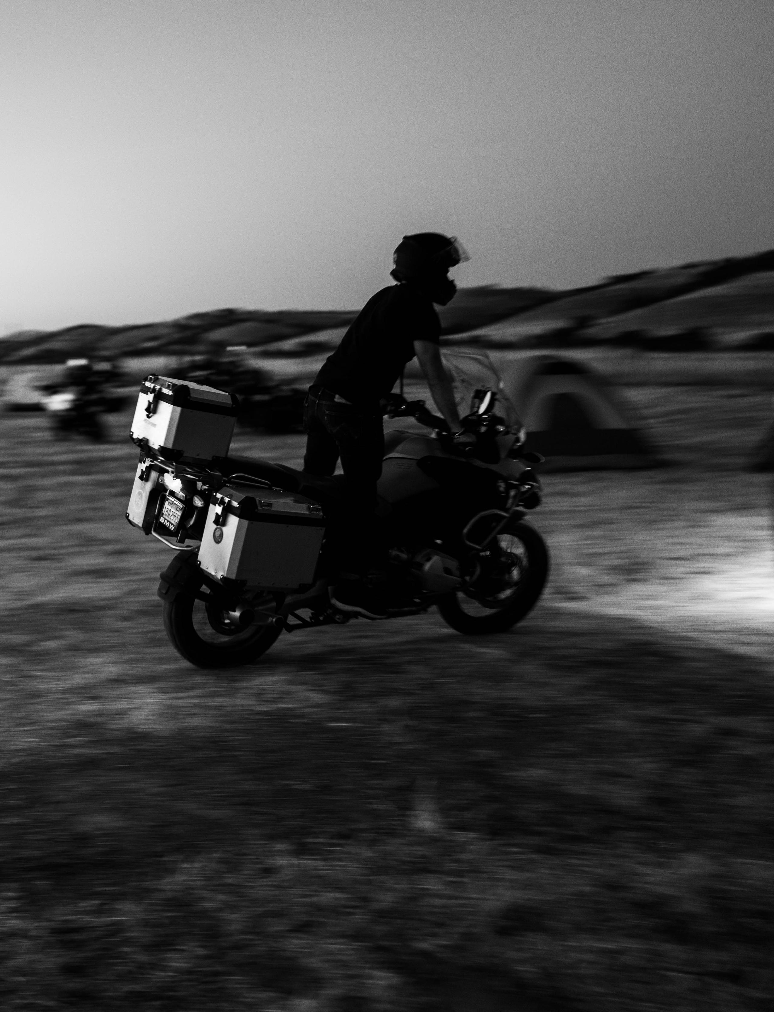 Black and white photo of motorcyclists riding through campsite at night