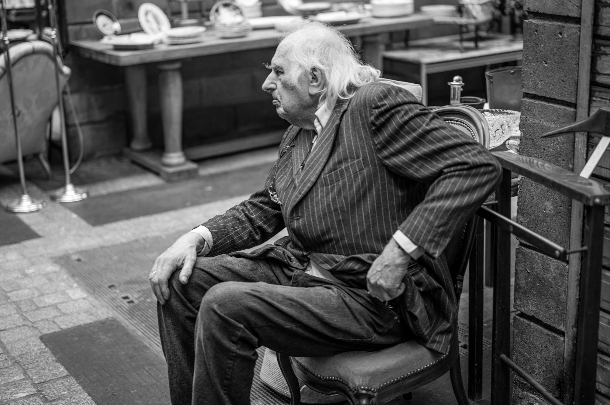 Elderly man in pin-stripe suit in Paris sitting on a chair