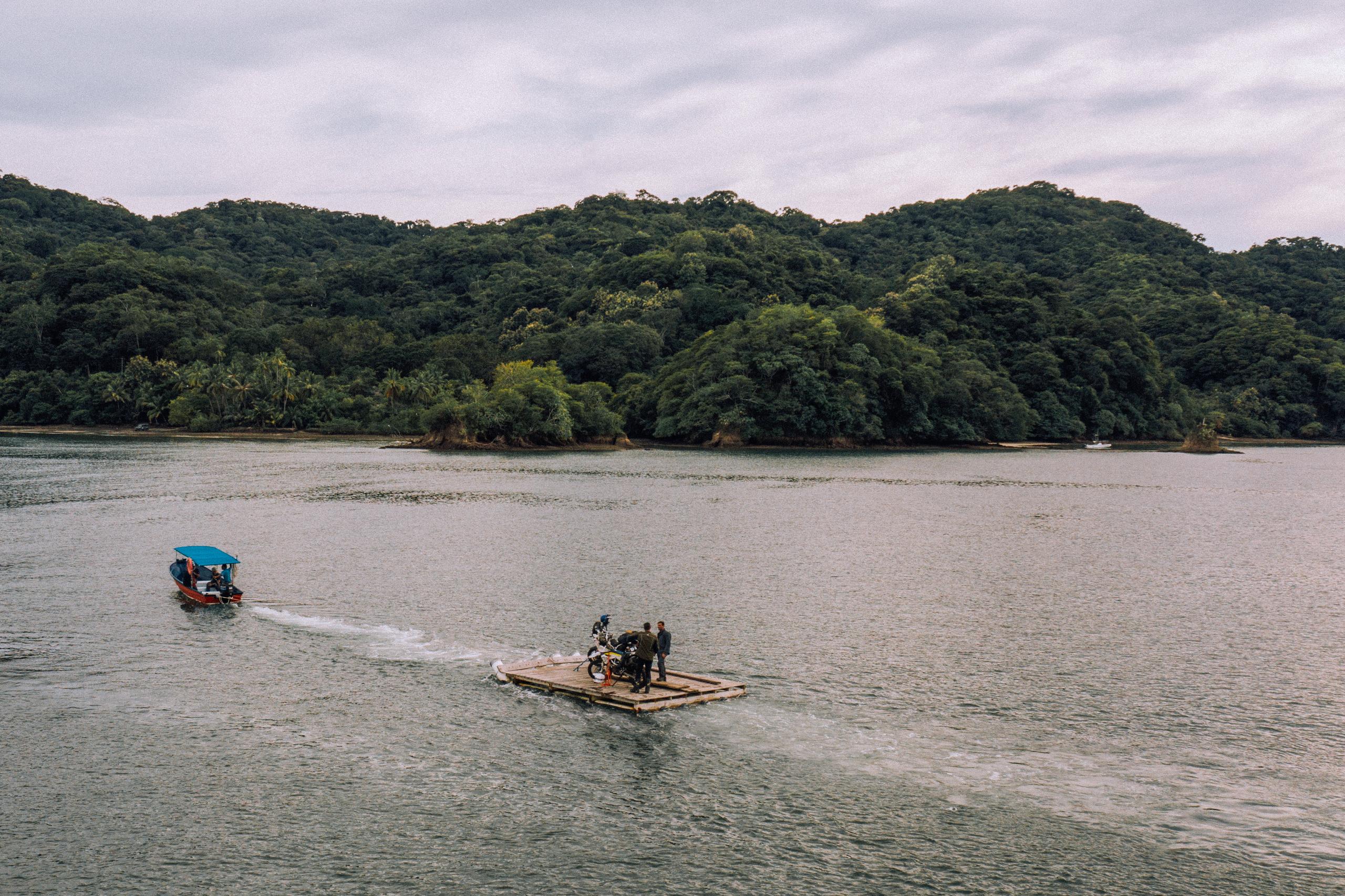 Two men with motorcycles on a wood raft being towed by a boat in the Gulf of Nicoya, Costa Rica