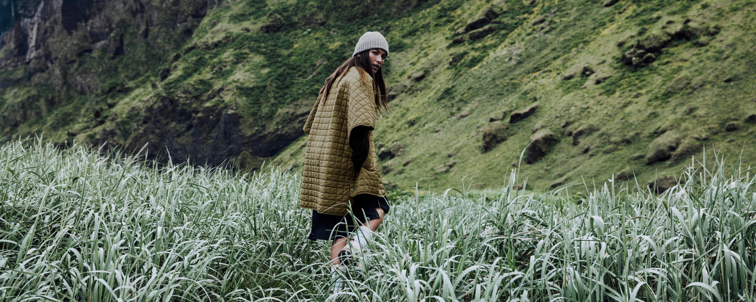 Woman walking through tall grass next to mountain in Iceland