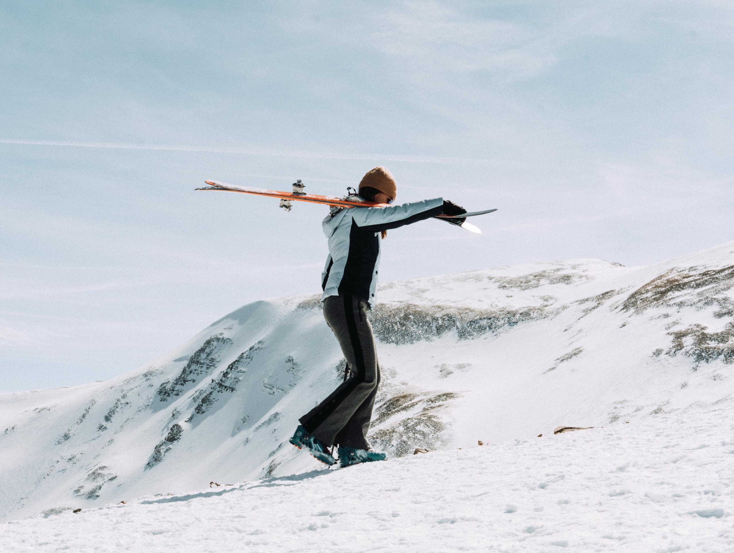 Woman holding skis walking up snowy mountain