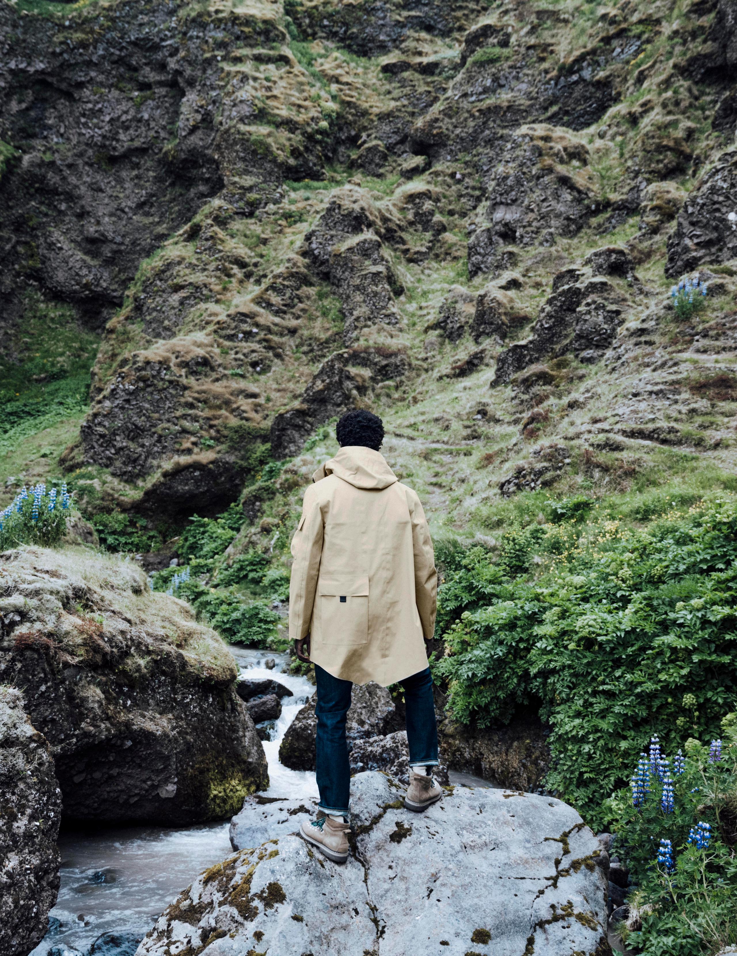 Back view of man wearing AETHER + Mackintosh Parka walking over river terrain in Iceland