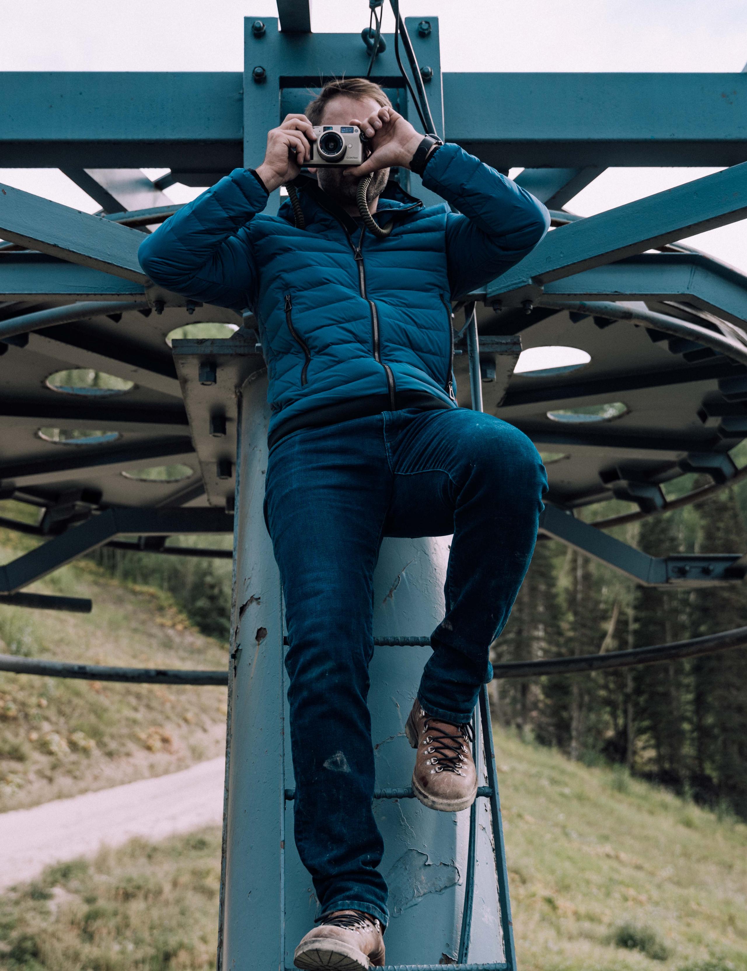 Man leaning on ski lift taking photo with point-and-shoot camera