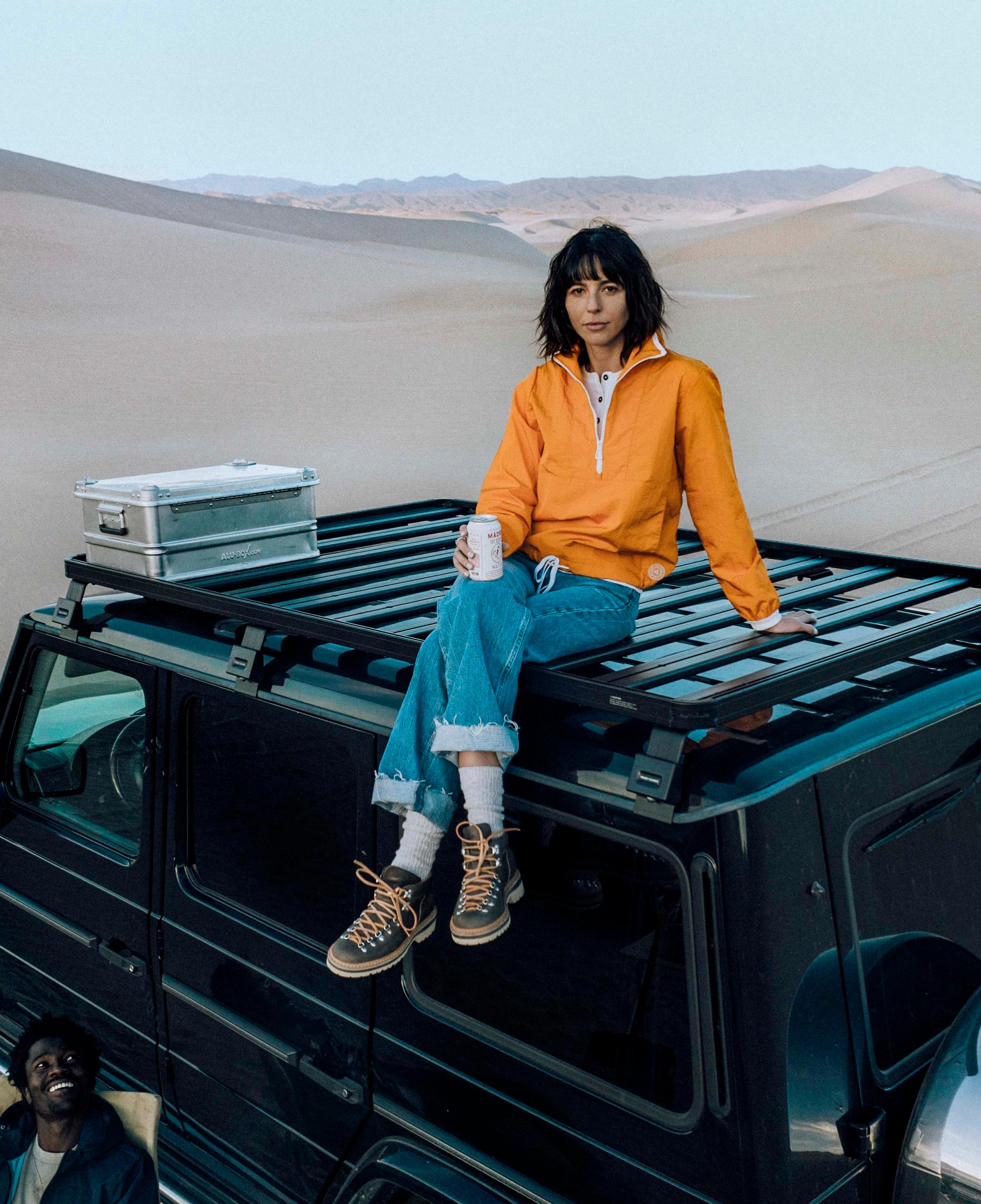 Woman sitting on top of black G wagon truck with sand dune landscape in background