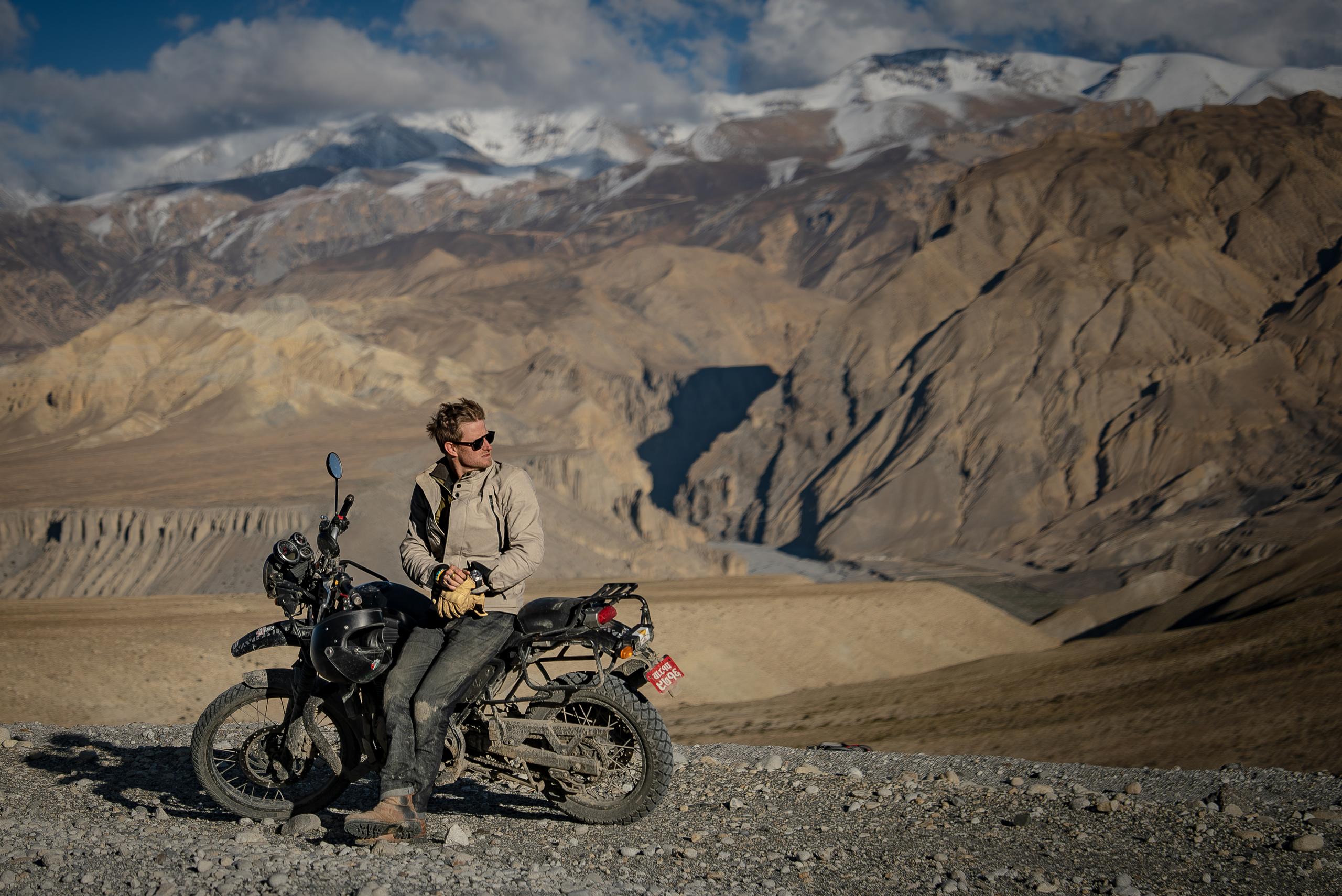 Cory Richards leaning on motorcycle on gravel road in Nepal landscape