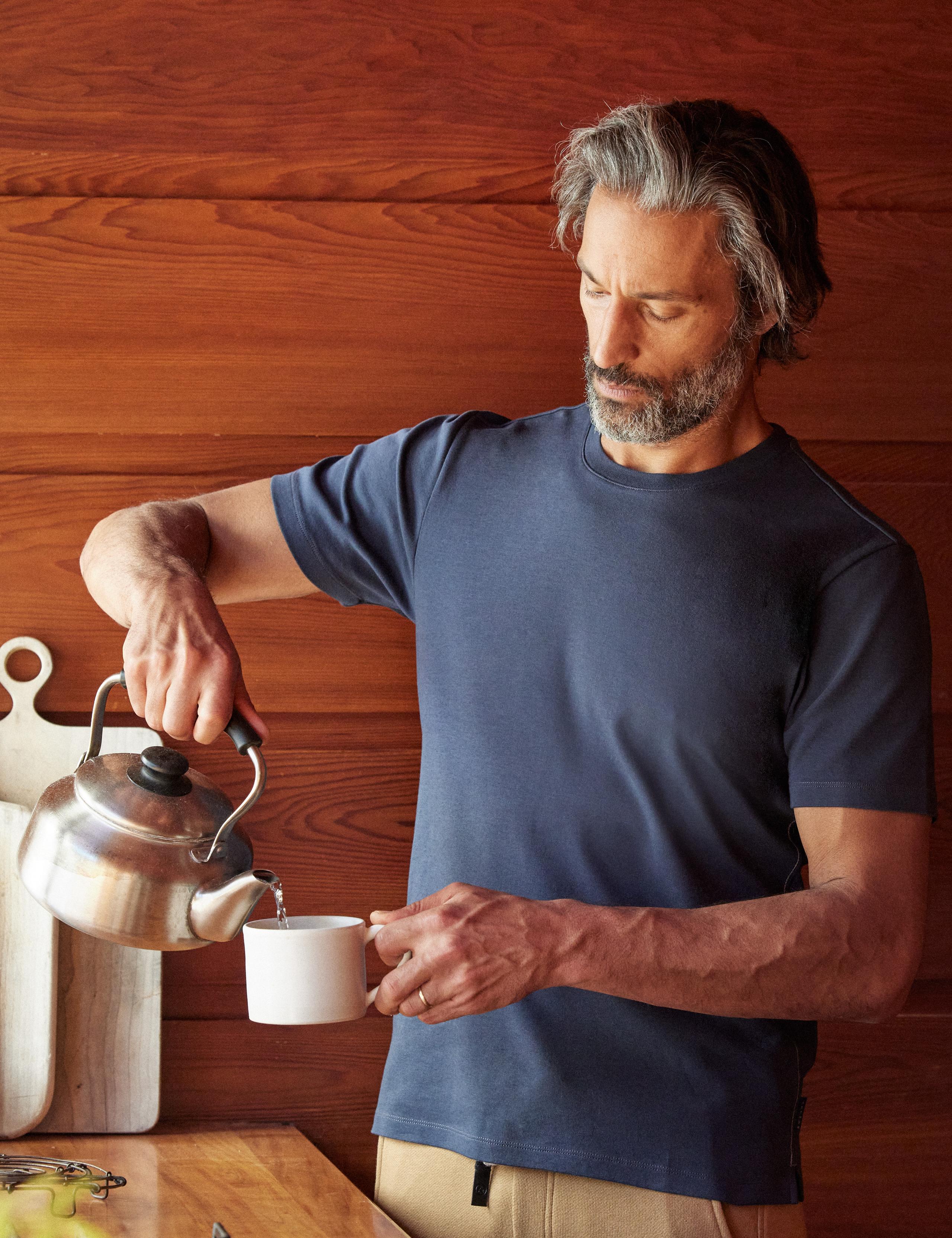 Man wearing Relaxed-Fit Crew Tee and pouring tea in kitchen of mid-century home