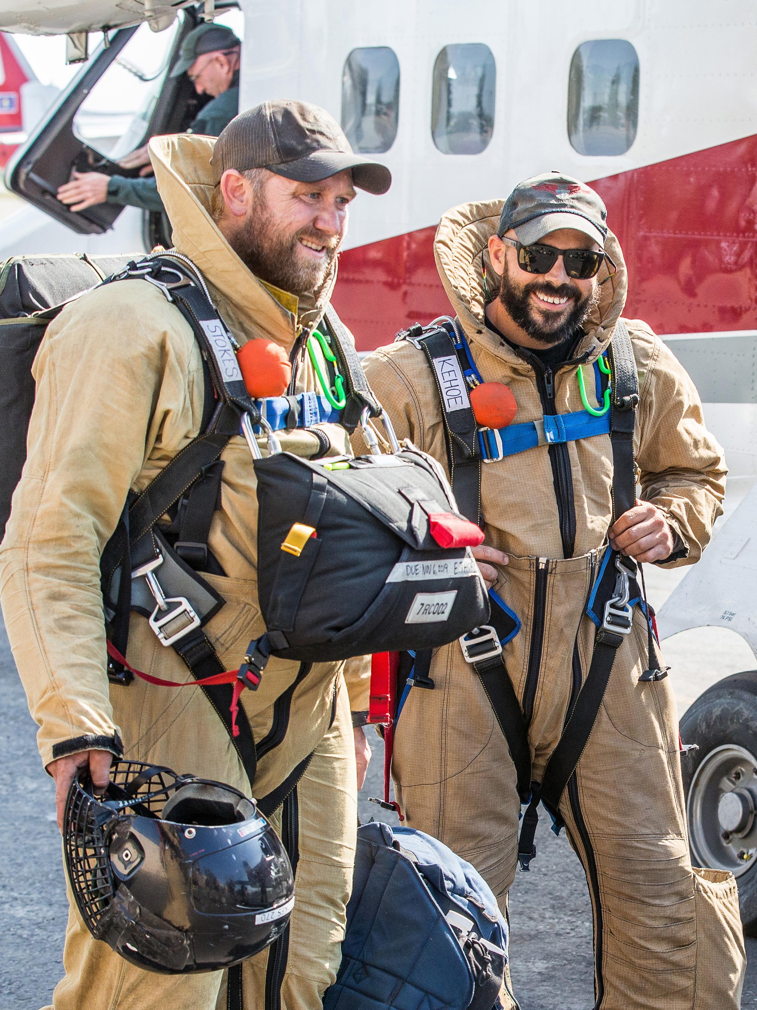 Two smokejumpers in full gear smiling alongside airplane