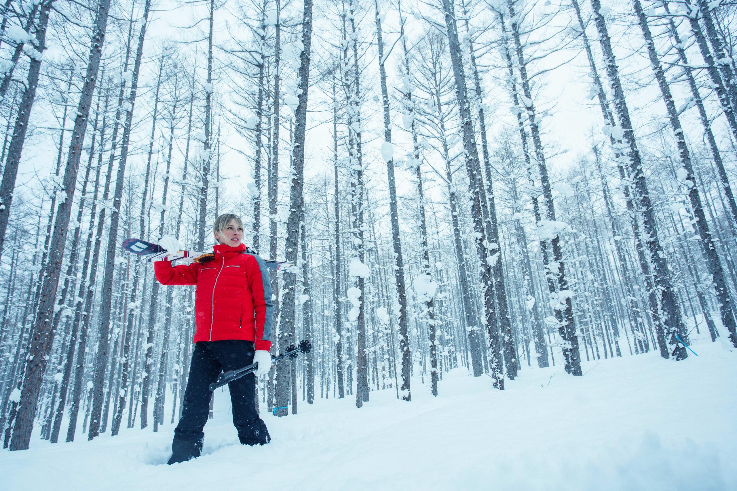 Woman holding skis in snowy forest in Hokkaido, Japan