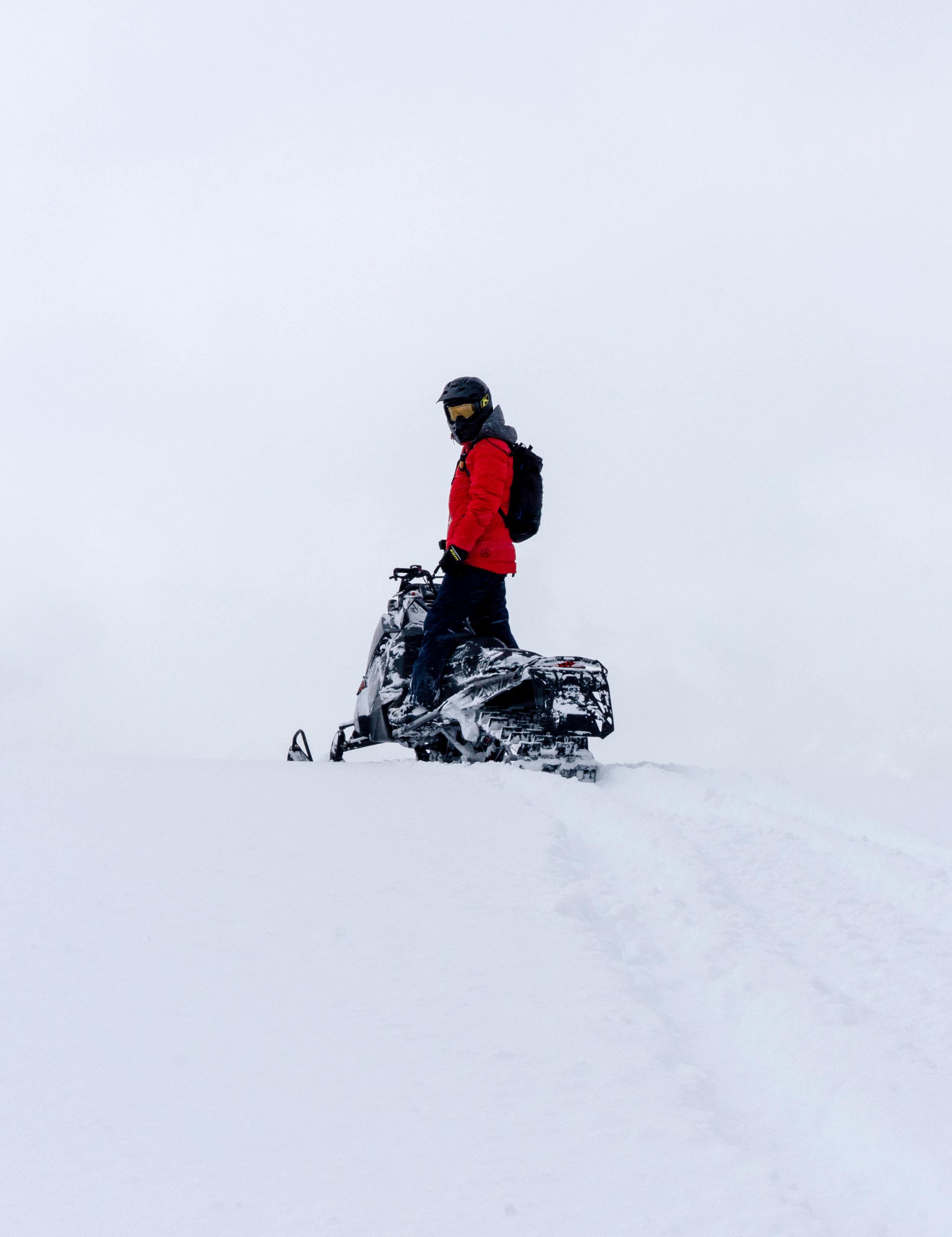 Man standing up on snowmobile looking back at the camera in full white-out conditions