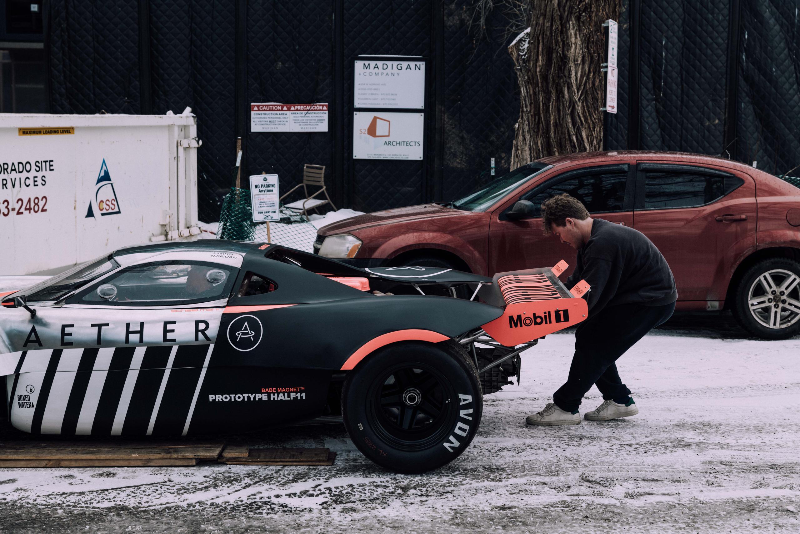 Man pulling race car prototype out of shipping container onto snowy road