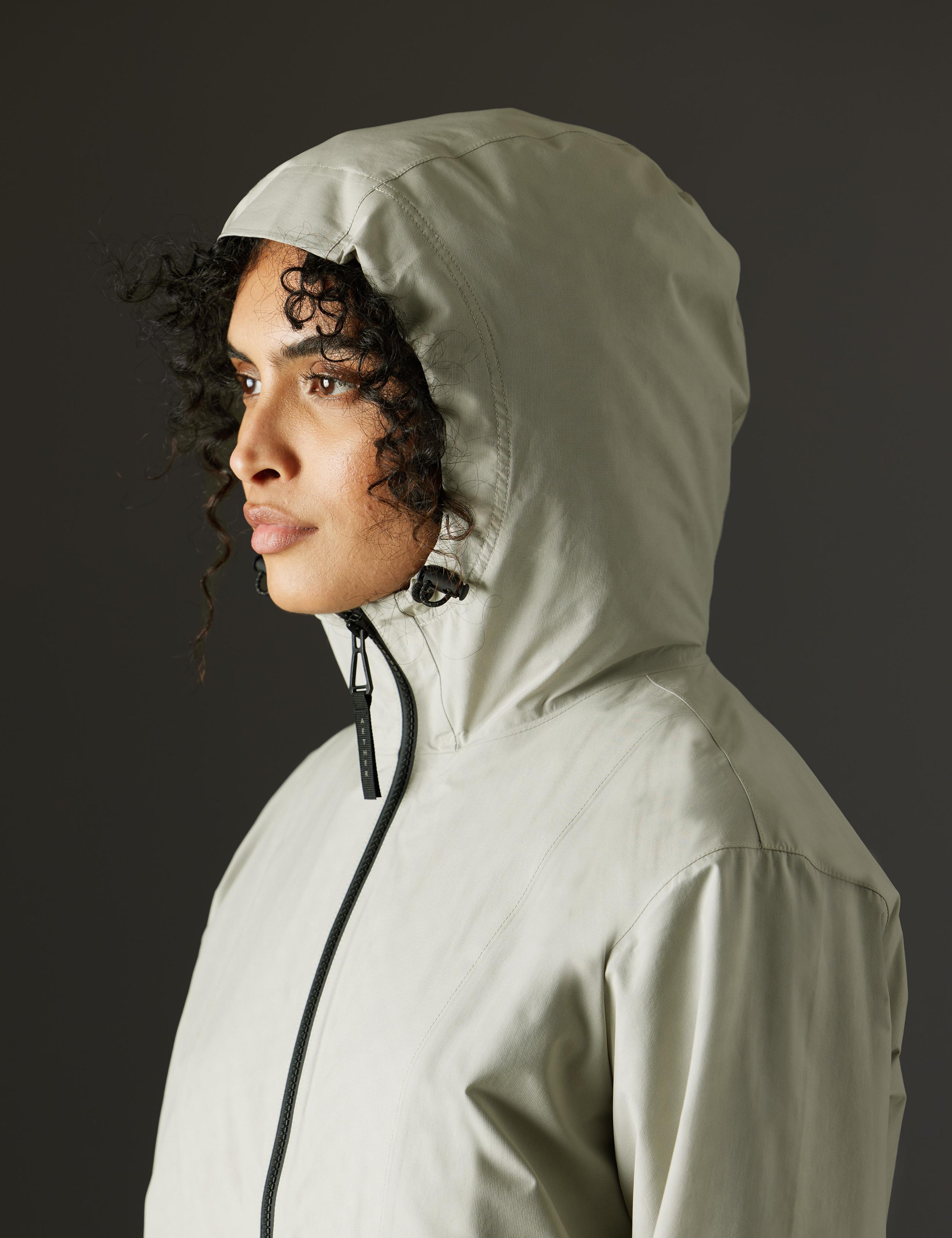 Woman in studio wearing the Kite Lightweight Jacket with hood up