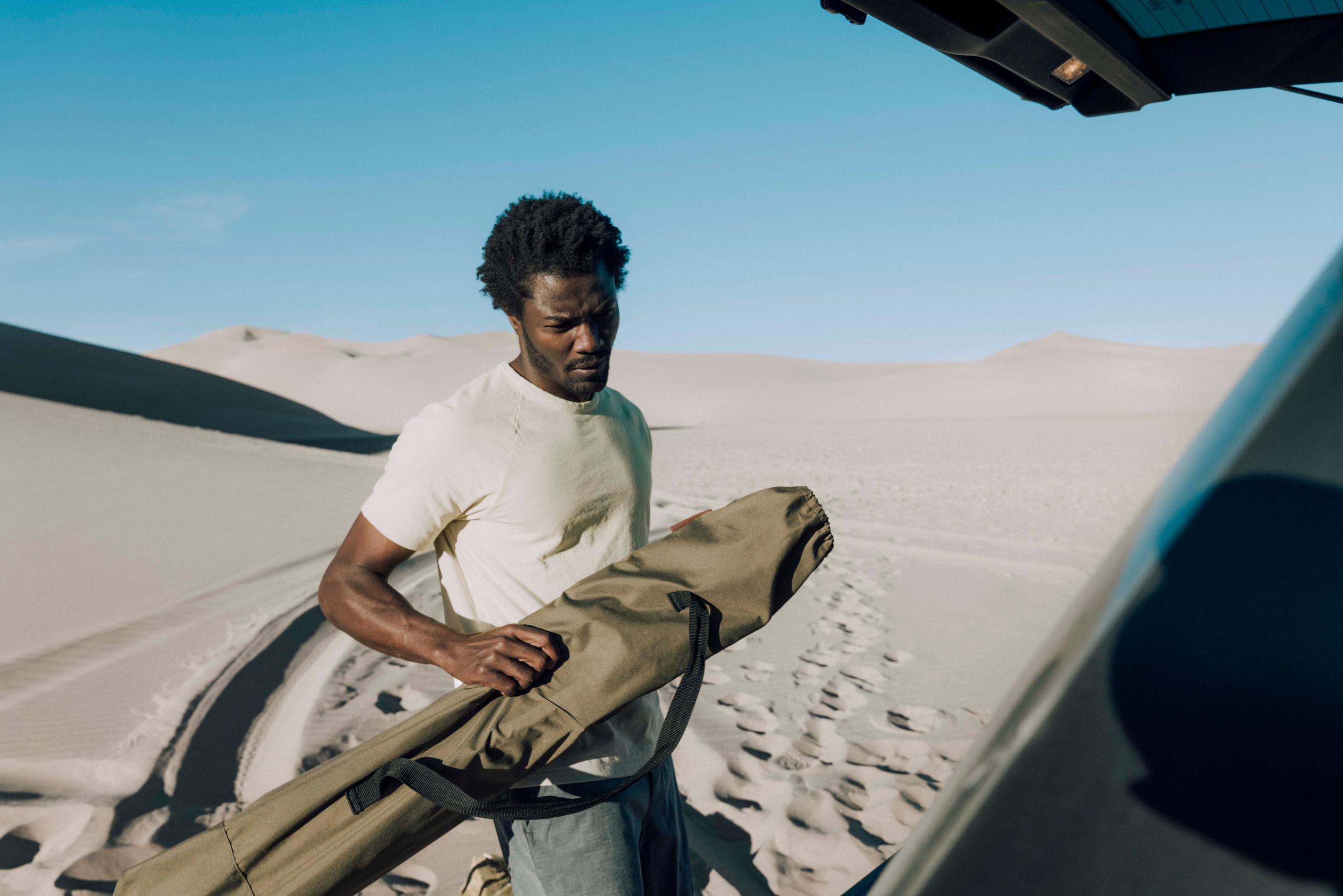 Man in t-shirt putting tent duffle into truck in the middle of sand dunes desert