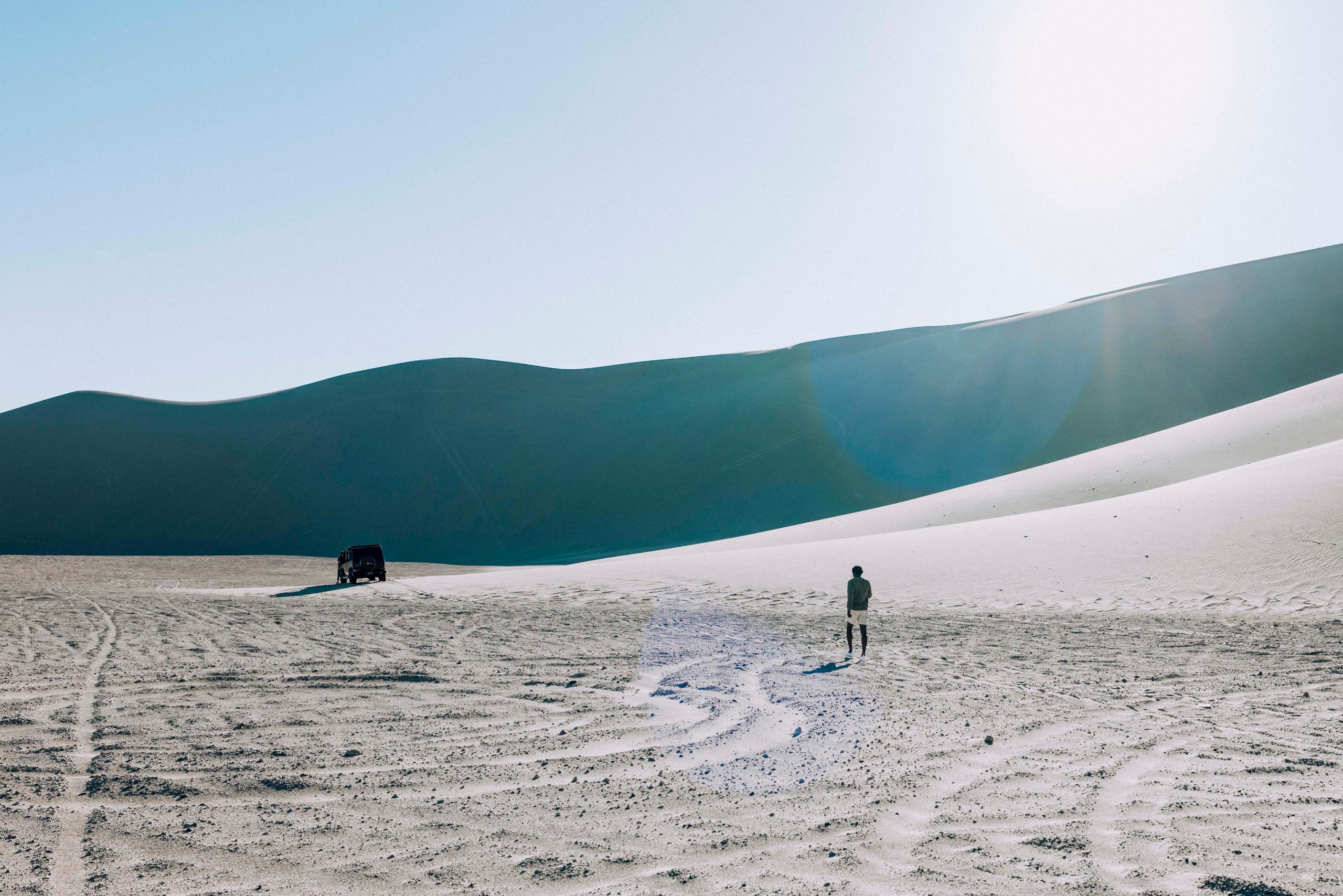 Man walking towards Land Rover amongst vast expanse of desert dunes