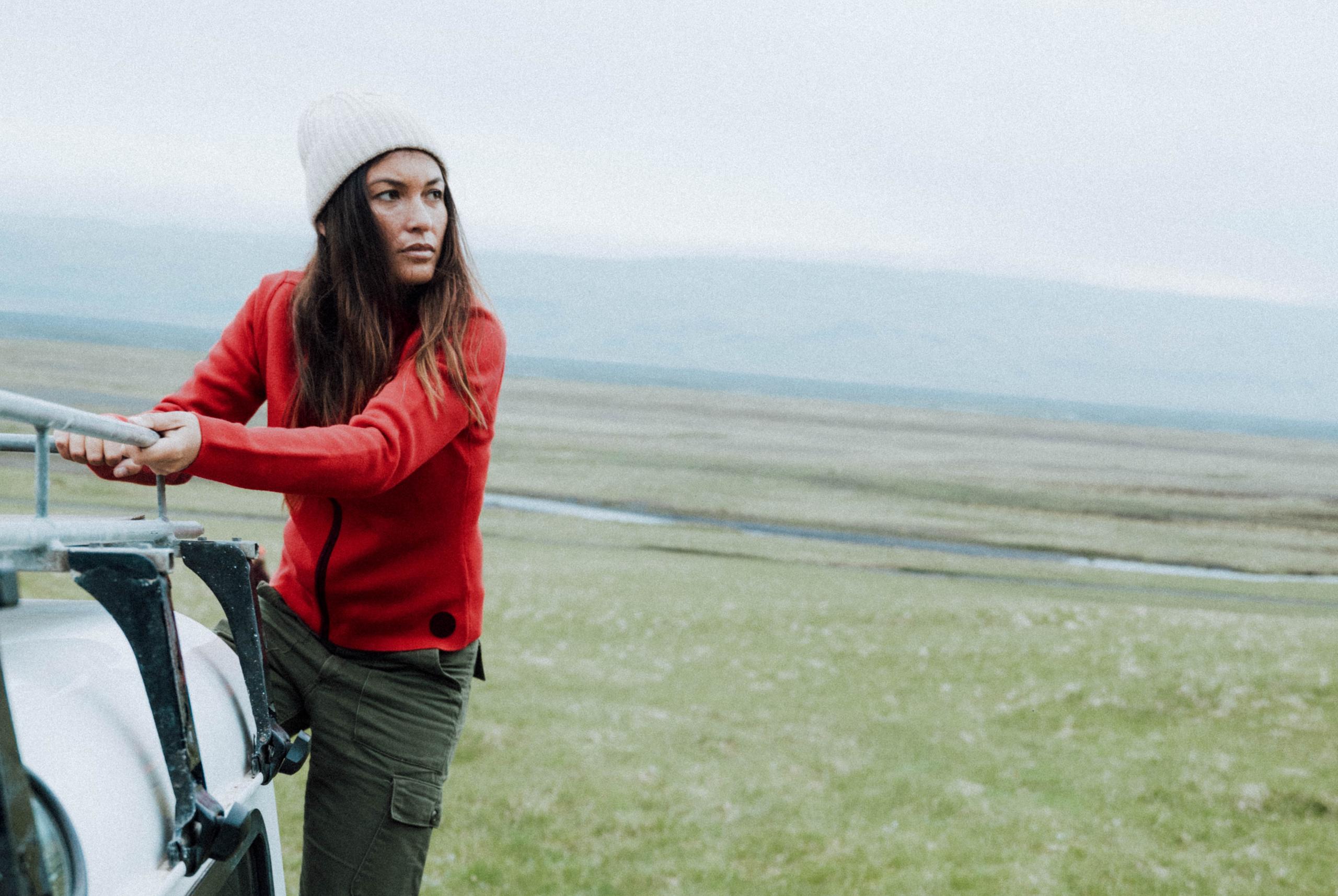 Woman wearing W Riley Full-Zip holding onto Defender vehicle rack with Iceland landscape in background