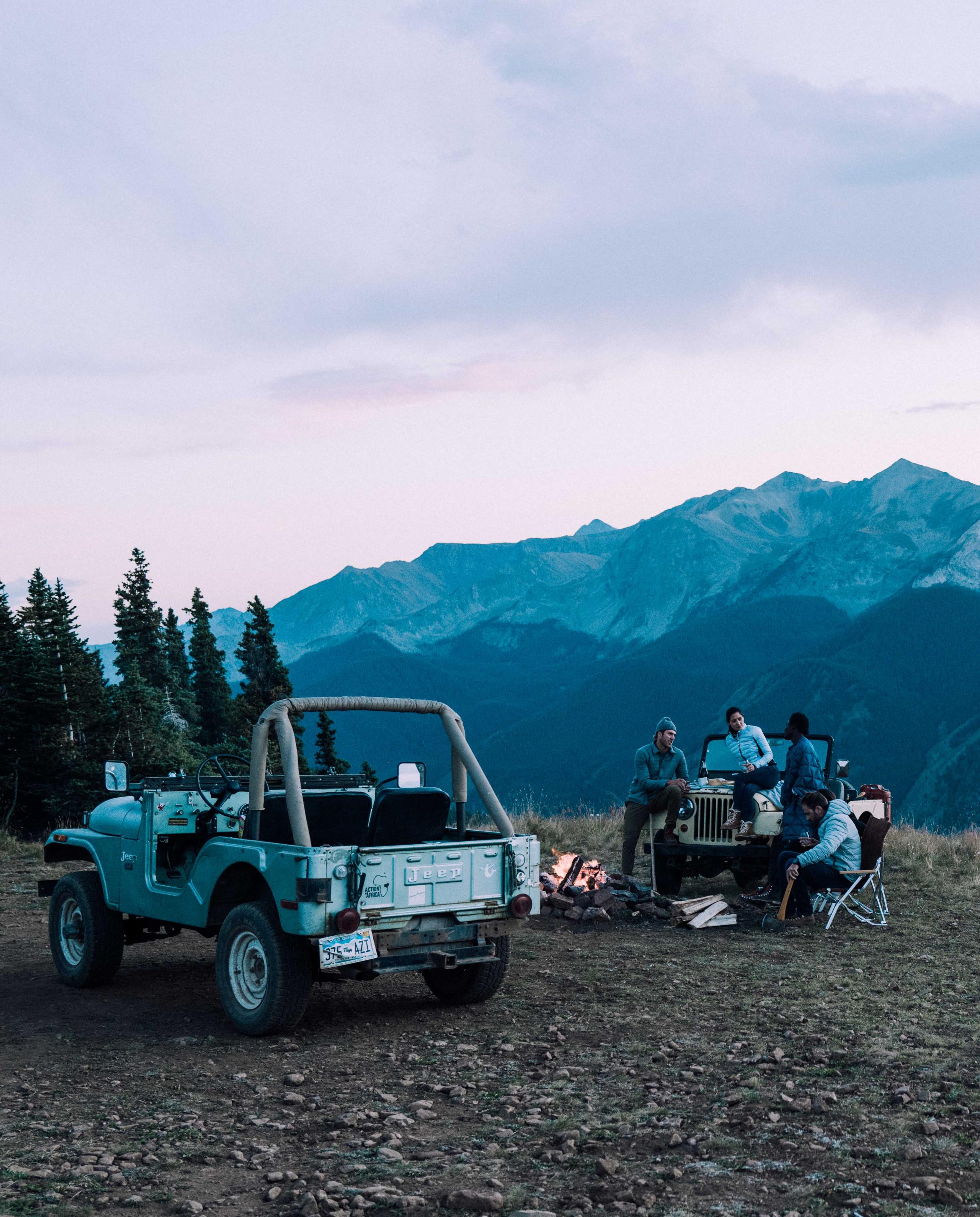 Four friends around campfire and vintage Jeep at dusk in Aspen mountains