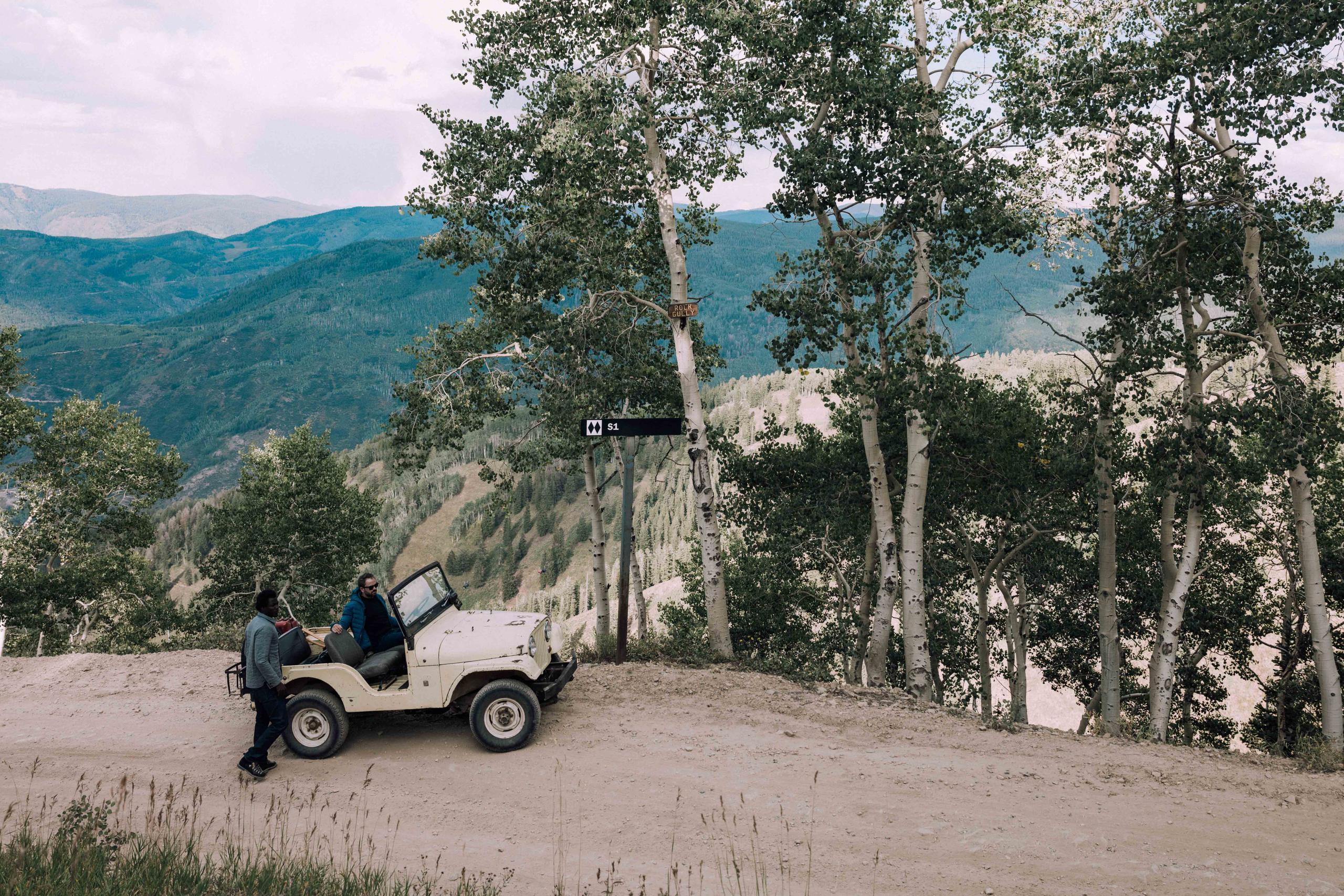 Aspen mountain landscape with two men in vintage Jeep on dirt road in foreground