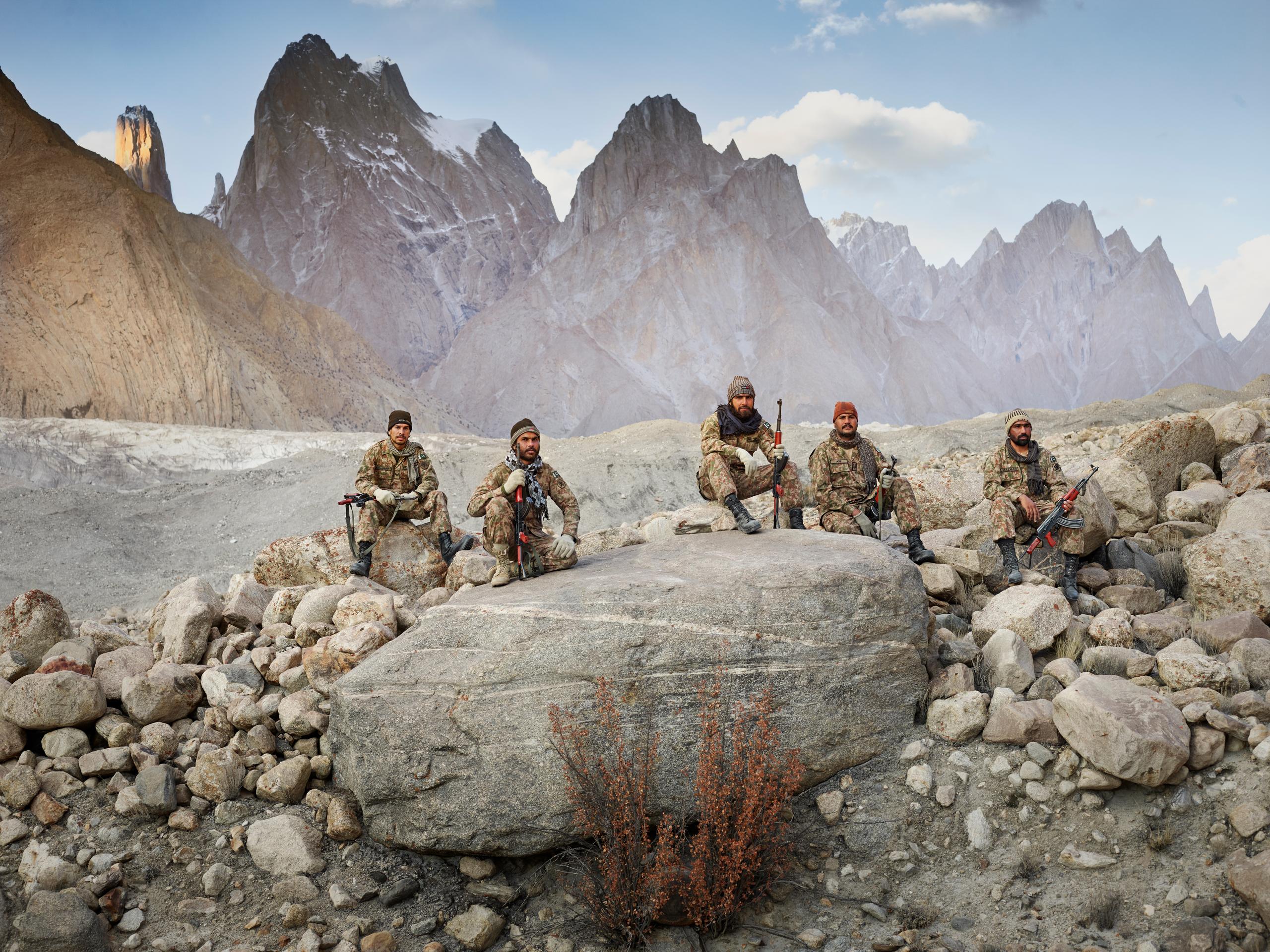 Camouflaged fighters with guns sitting in rocky landscape in Pakistan with mountains behind them