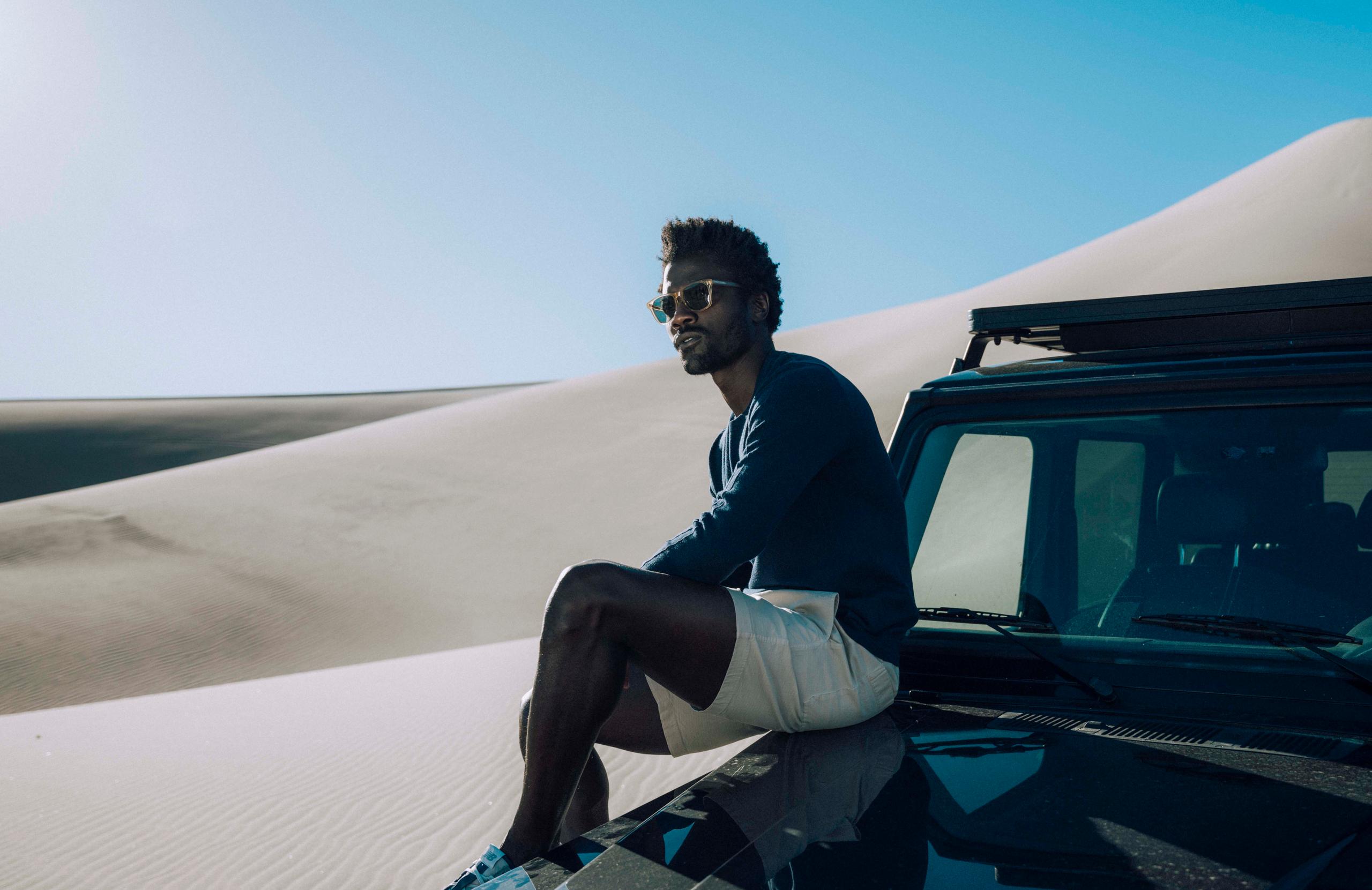 Man sitting on truck in middle of sand dunes landscape