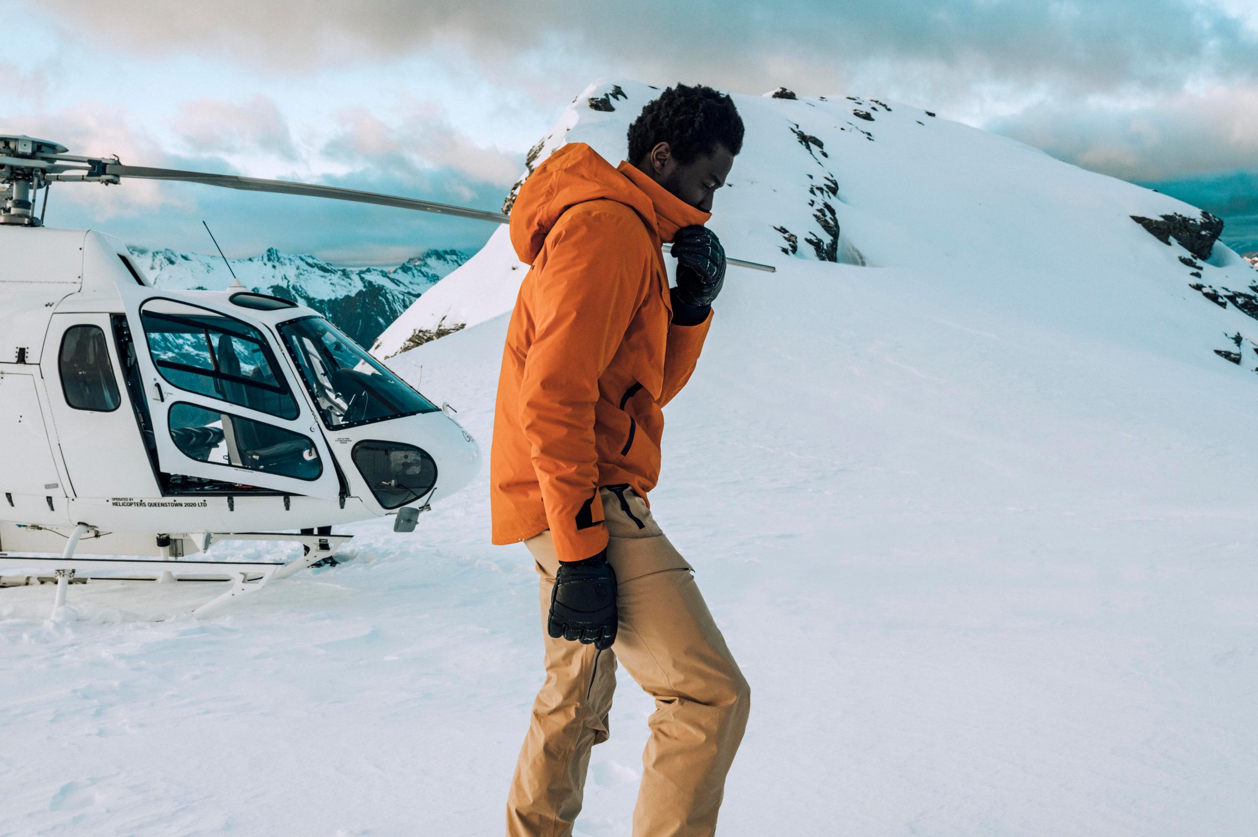 Men in Brighton Insulated Snow Jacket walking in front of a helicopter on snowy mountain.