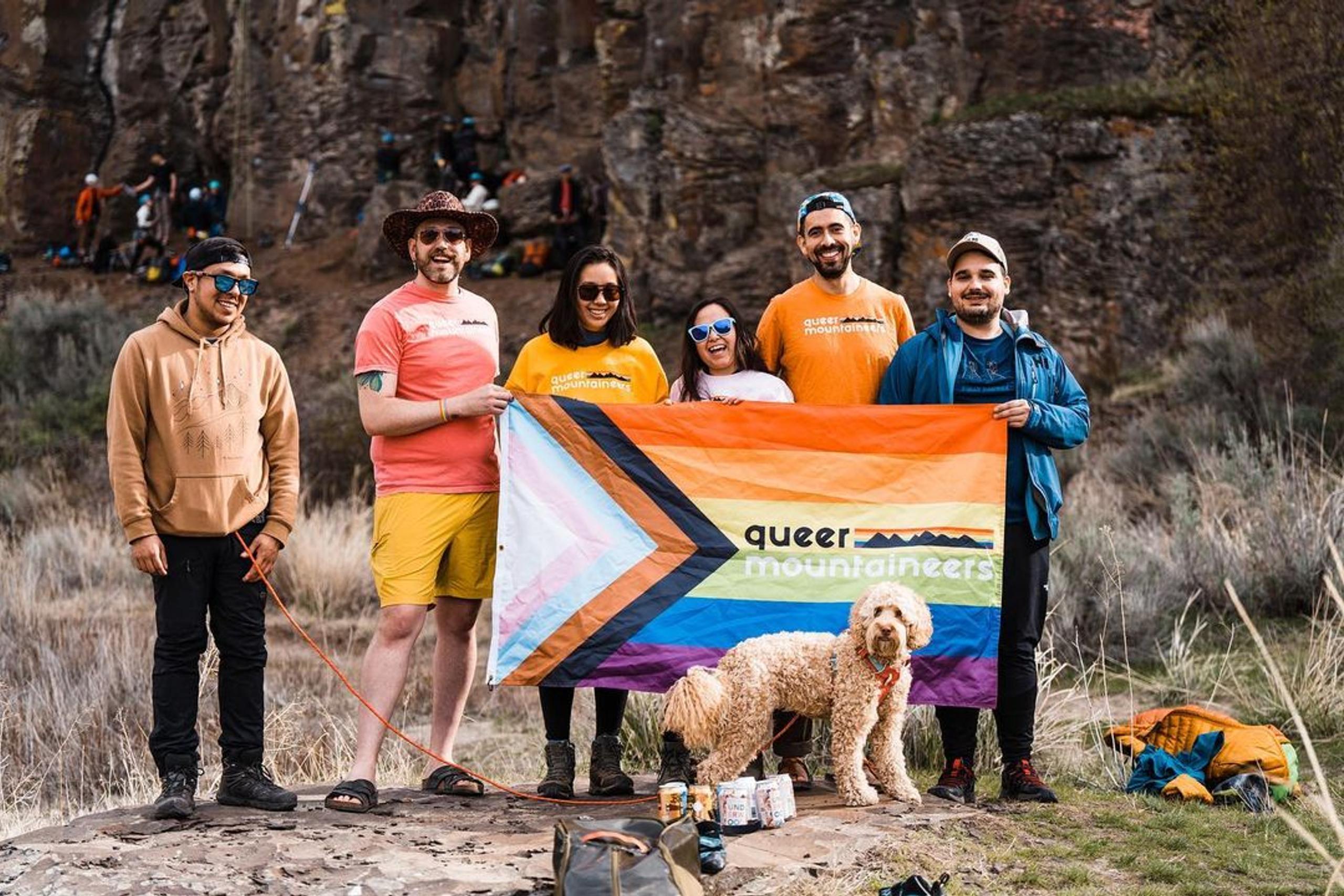 Group of people and dog holding Queer Mountaineers flag in front of The Feathers